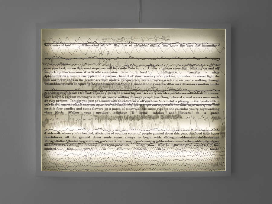 A white light box hanging on a wall with a scroll of text.