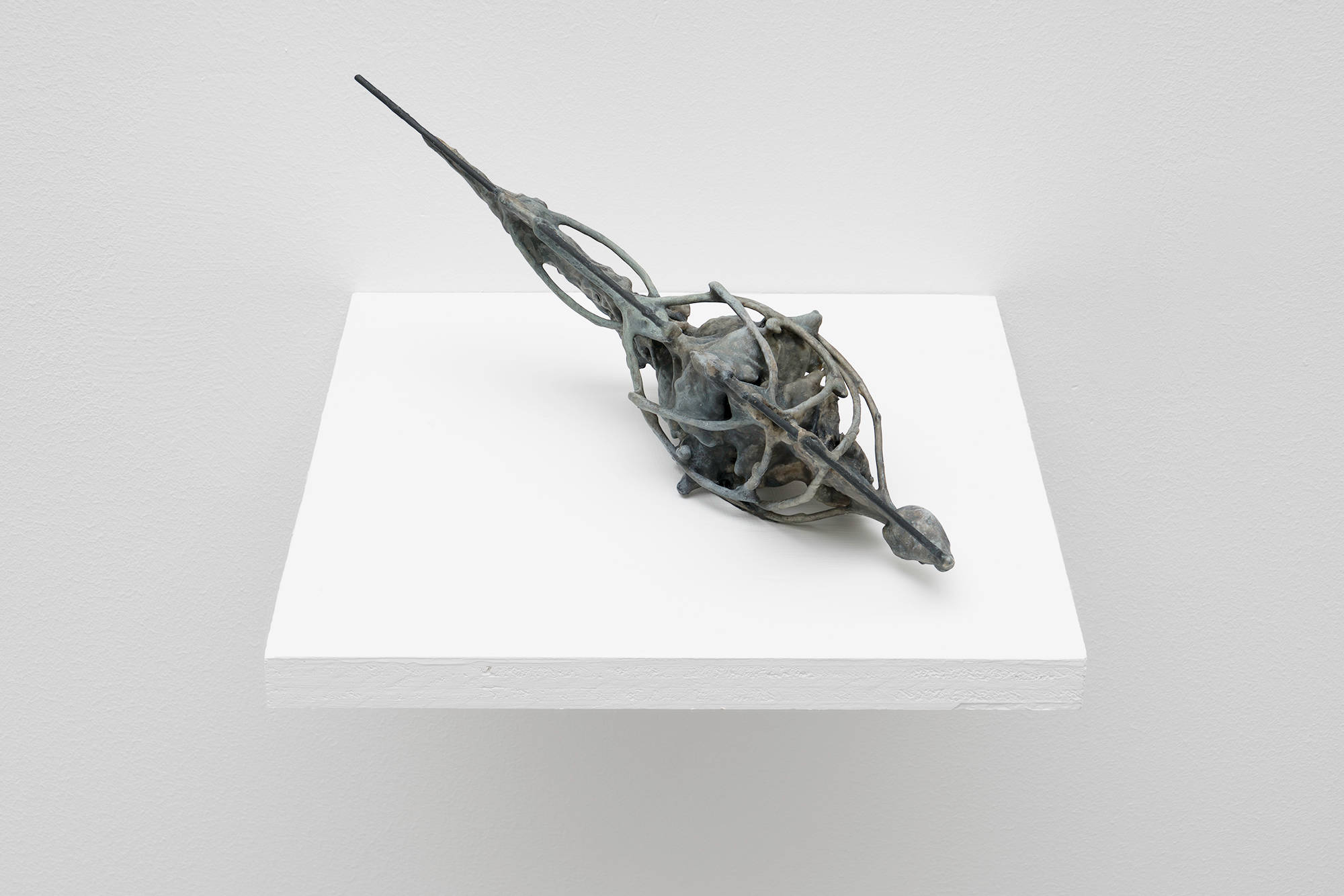 A grey, abstract sculpture by Matt Hoyt sits on a white shelf. The sculpture is highly textured and wiry. It resembles an surgical instrument of some kind.