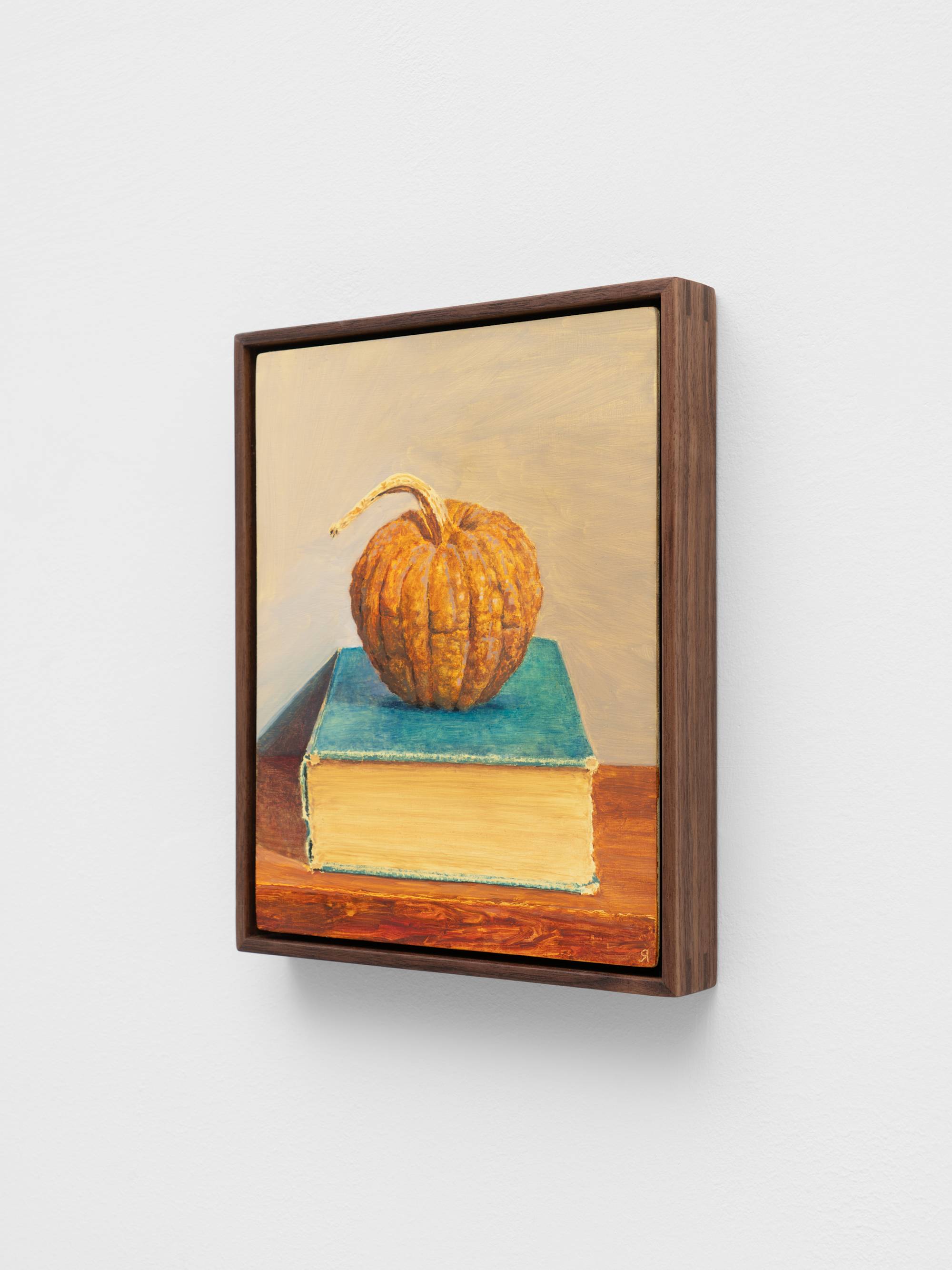 A small, dark wood framed painting of a squash sitting atop a thick and weathered blue book.