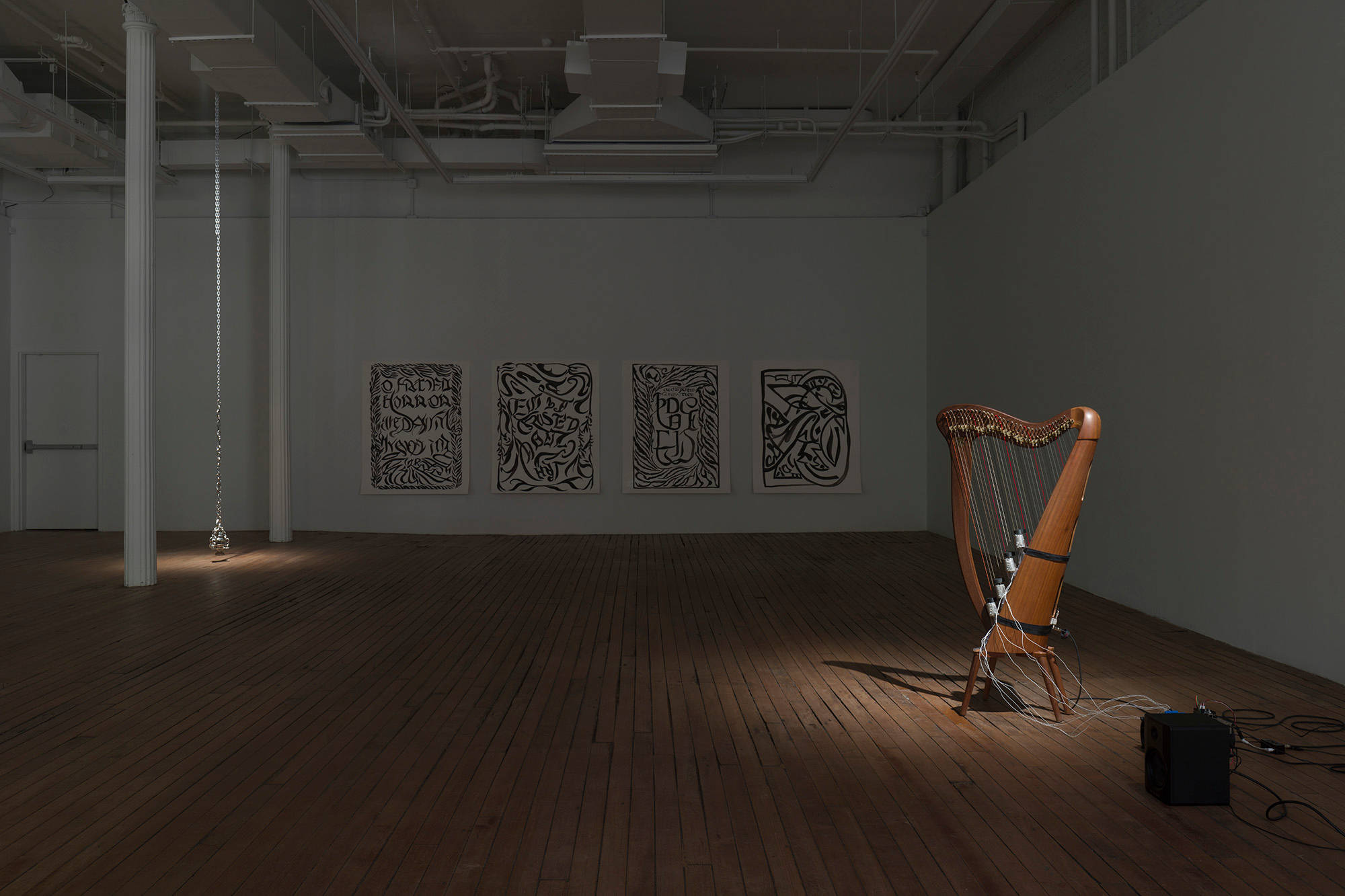 A large, dark gallery with 4 drawings, a self-playing harp, and a pewter thurible suspended from the ceiling with a chain. Spotlights shine on the harp and the thurible.
