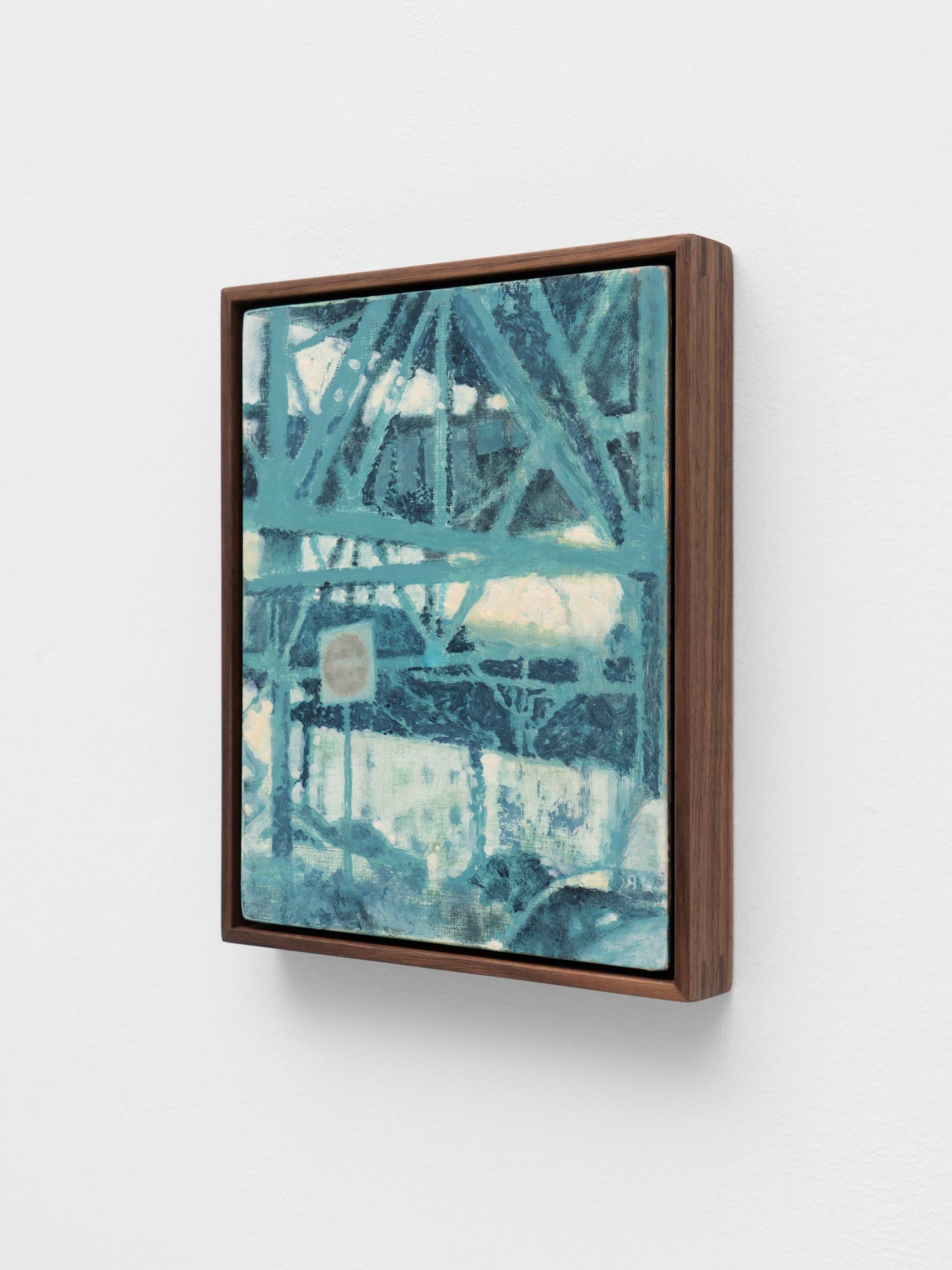 A small, dark wood framed painting of an intersection under suspended train tracks hangs on a white wall.