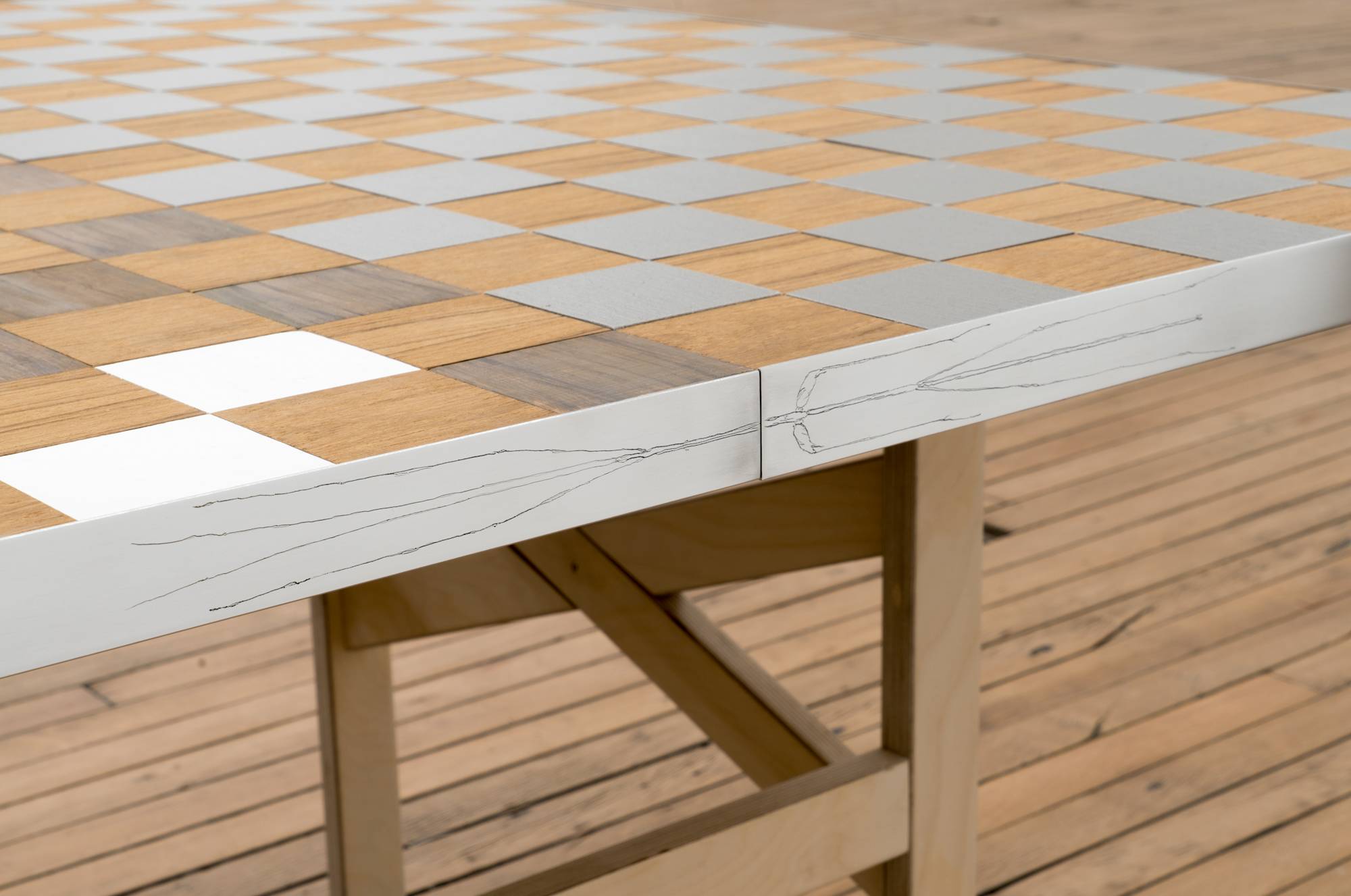 Detail of Ian Miyamura plywood table sculpture featuring a checkerboard top and removable leaf painting of depicting the letters "T, A, S, T, E" arranged at different sizes and angles on a light grey background.