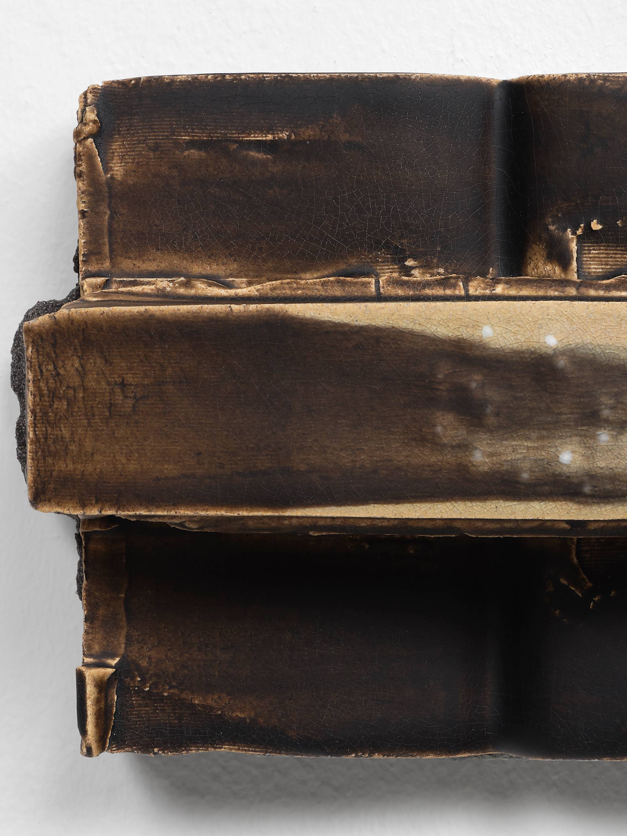 Detail of a small, brown, ceramic sculpture featuring two vertical cuboids with a long horizontal band stretching the full width embedded with a circle of white beads.