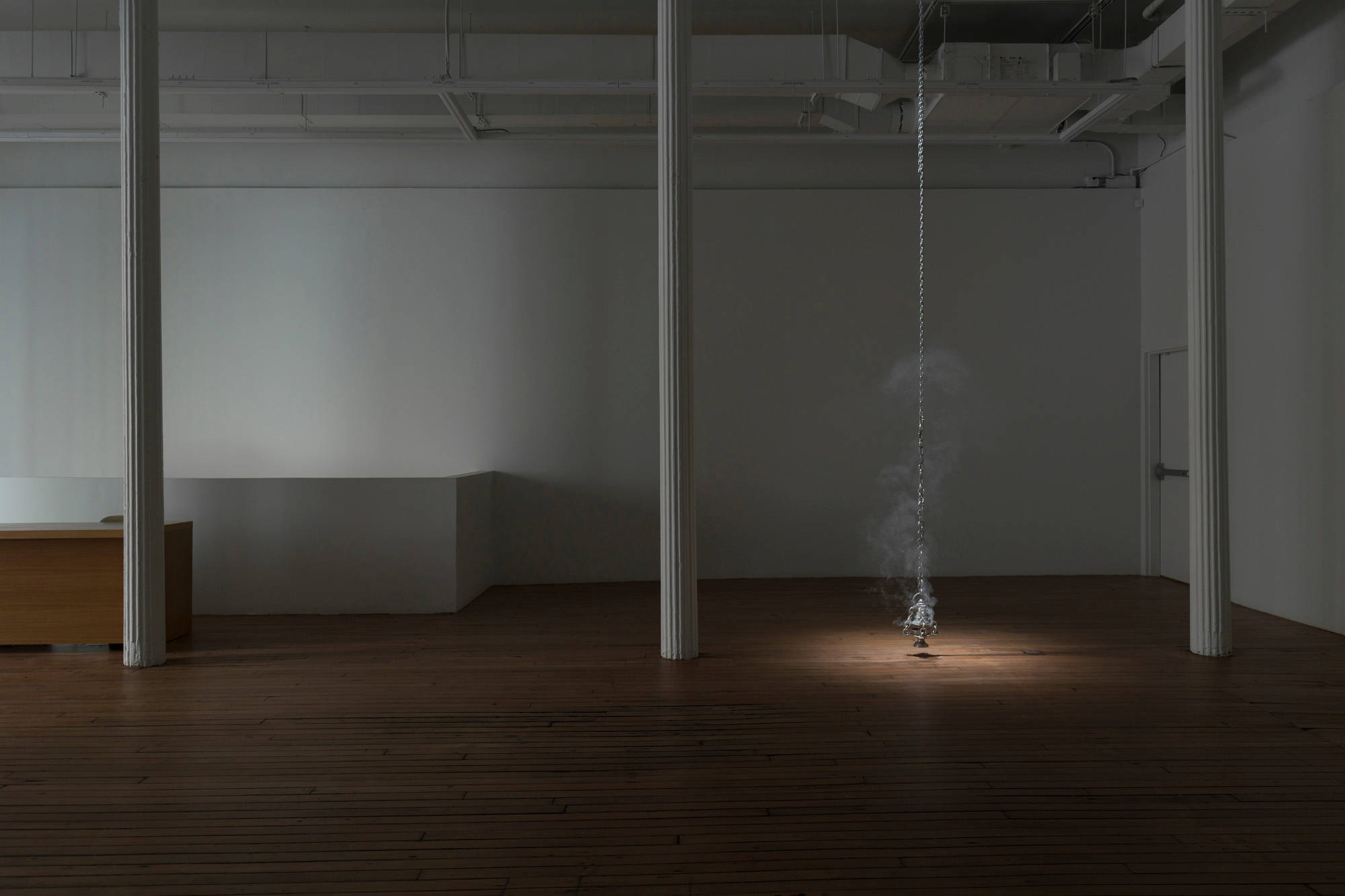 A pewter thurible burning incense hangs from a chain from the ceiling of a dark art gallery.