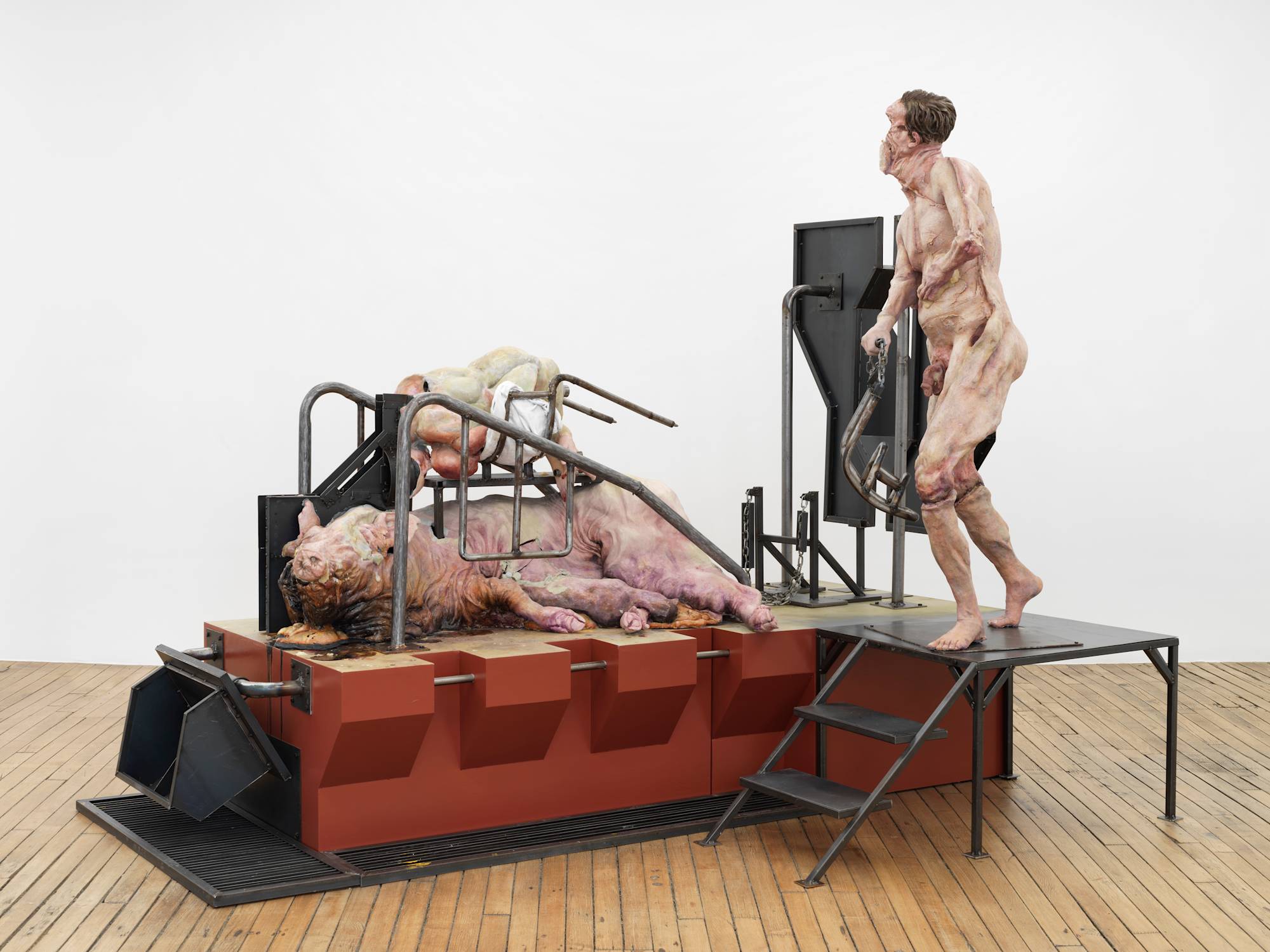 A monumental sculpture made primarily of steel and wood. Atop the base of the sculpture is an abstracted human form and a large pig.