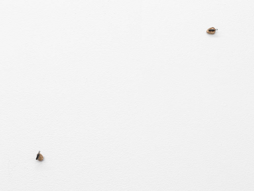 A white gallery wall with two miniature objects attached to it resembling technical equipment.