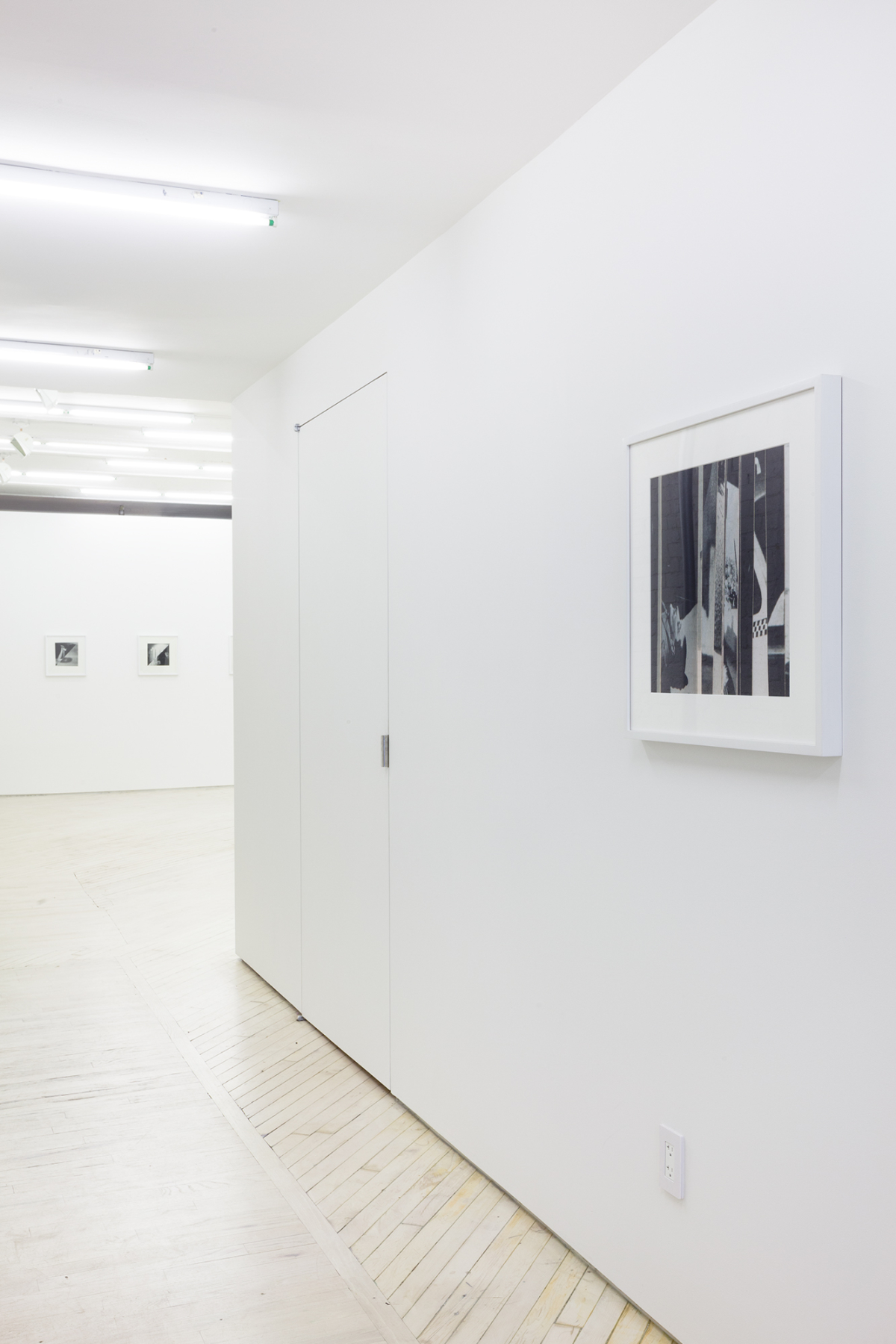Image of Bureau's white painted hallway with a black and white framed photograph in the foreground and two smaller photographs at a distance inside the main space.