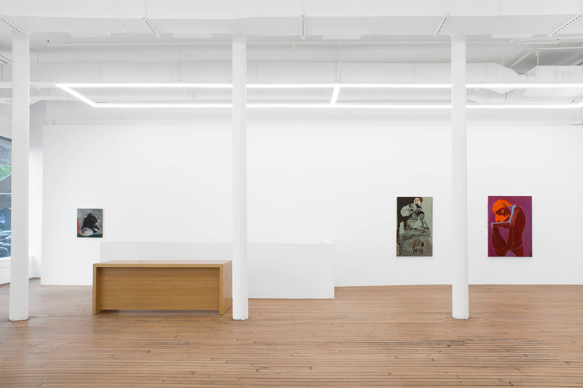Three paintings hang on the east wall in the upstairs of the gallery. A painting of a head hangs to the left of the entrance to the stair case. To the right hang the other two paintings. One of multiple figures against a green background, the other a solitary figure against a pink background.