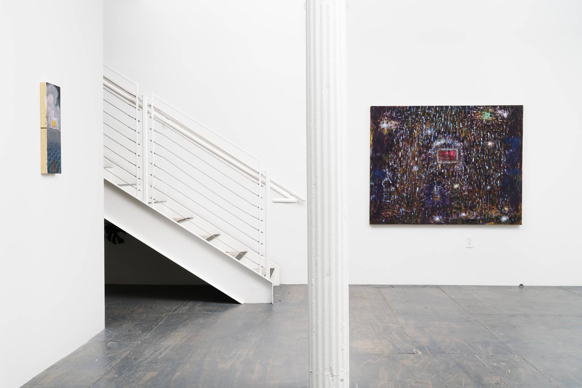 A dark blue abstract painting with sparkly details hangs on the east wall of the gallery. The painting sits to the right of a white column that dissects the room. To the left of the column, a staircase ascends out of frame. To the left of the stairs a small blue landscape diptych hangs on the wall.