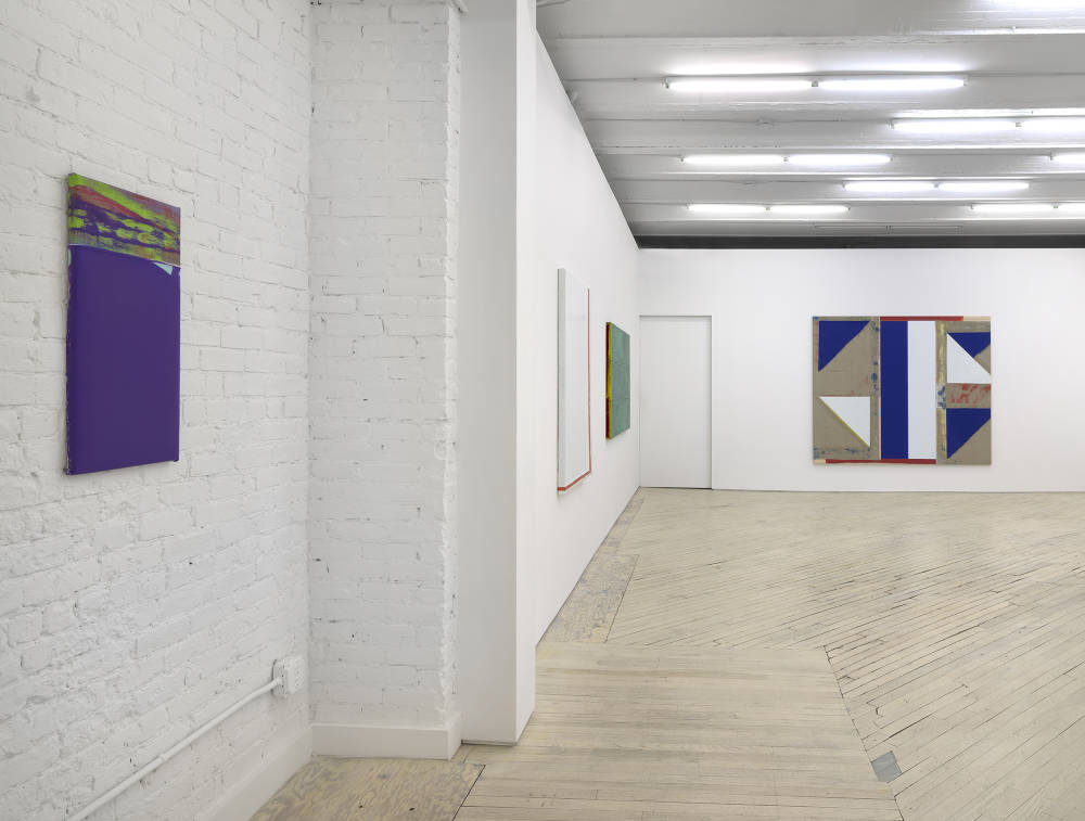 Along a gallery wall, a small purple painting installed next to a larger monochromatic white painting next to a green painting. On the back wall is a larger abstract painting consisting of blue, white, red, and brown areas. 