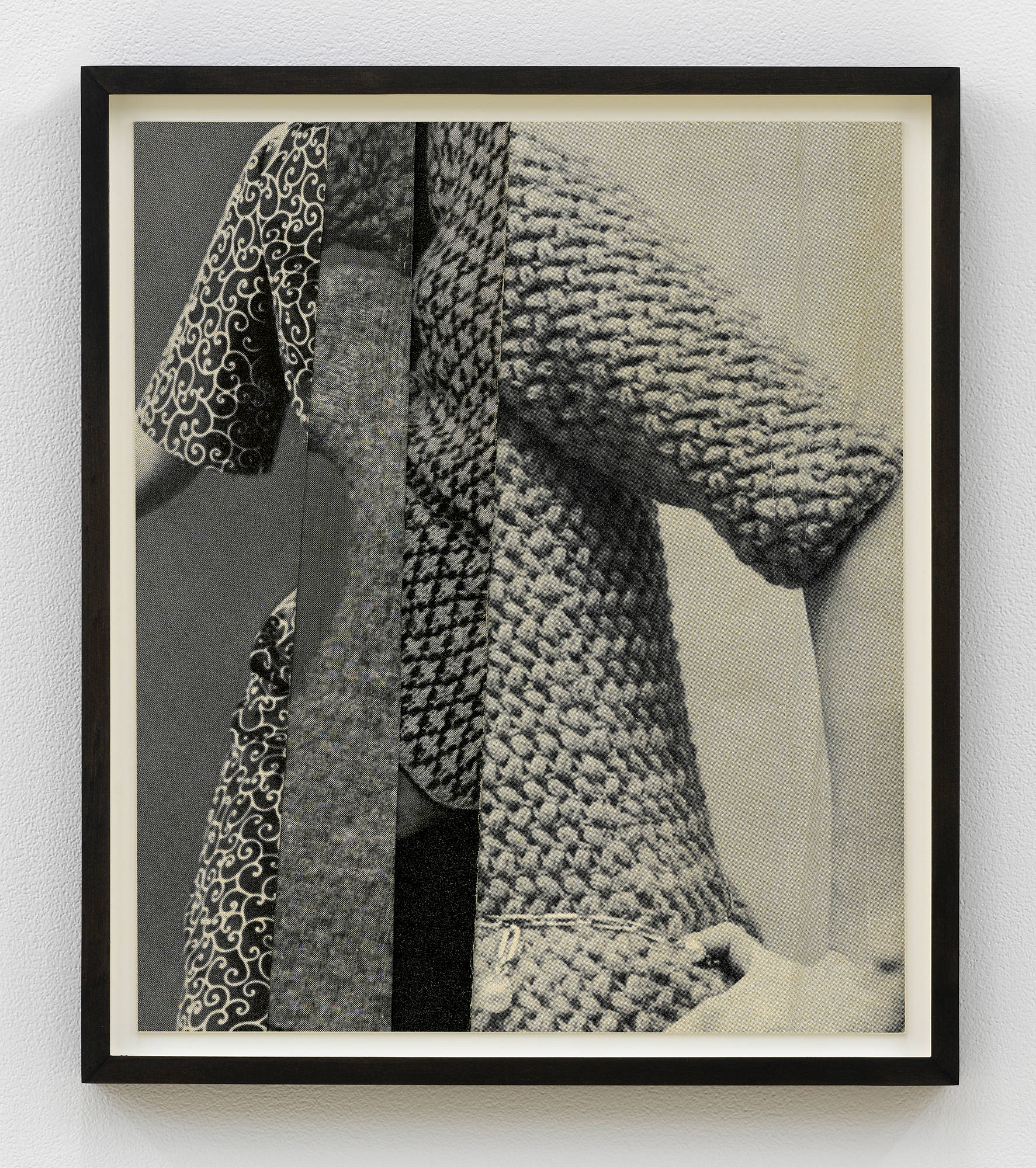 A gray scale photograph depicting collaged human forms and clothing garments in a dark brown wood frame.