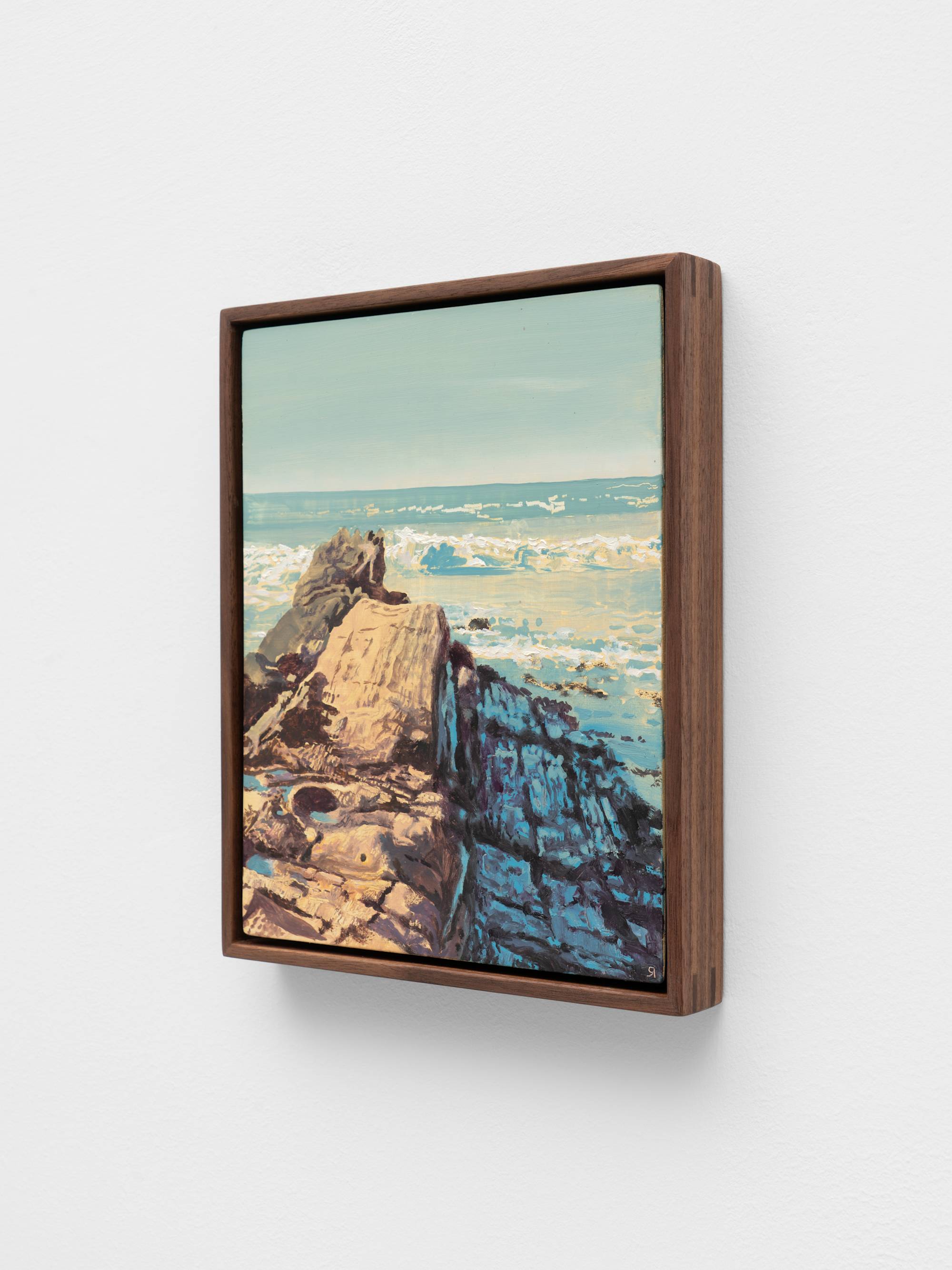 A small, dark wood framed painting of a rock formation jutting out into the sea.