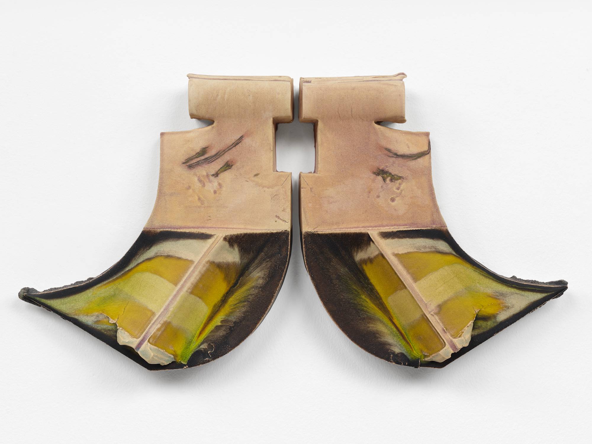 Two ceramic sculptures hang on a wall mirroring each other. The two pieces resemble the letter "J", one forwards, one backwards. A spine runs diagonally down each bottom swoop, striped with yellow and green glaze, against a background of dark brown glaze.