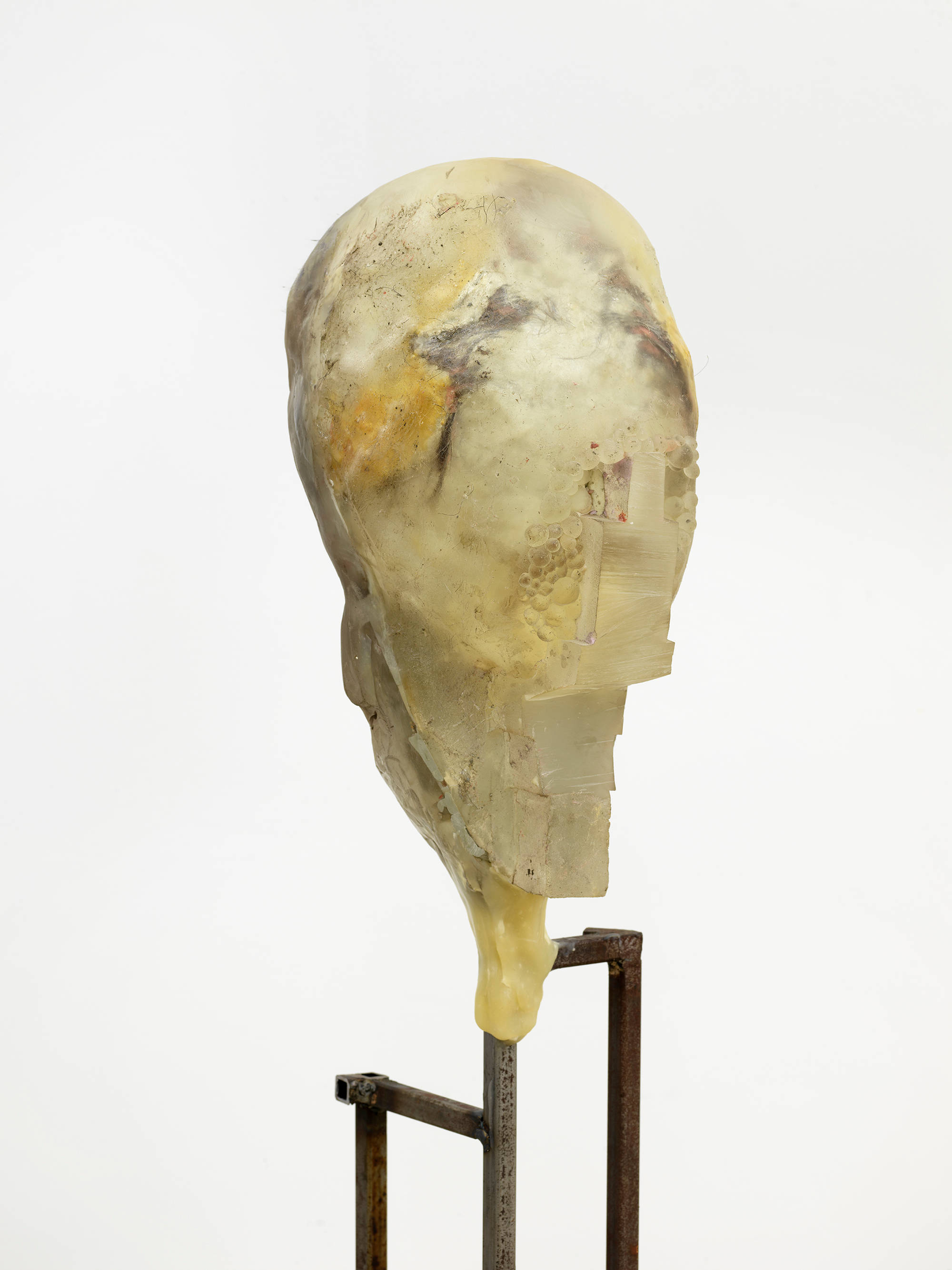 In a gallery space, a detail of an abstract sculpture resembling a human form with a steal base.