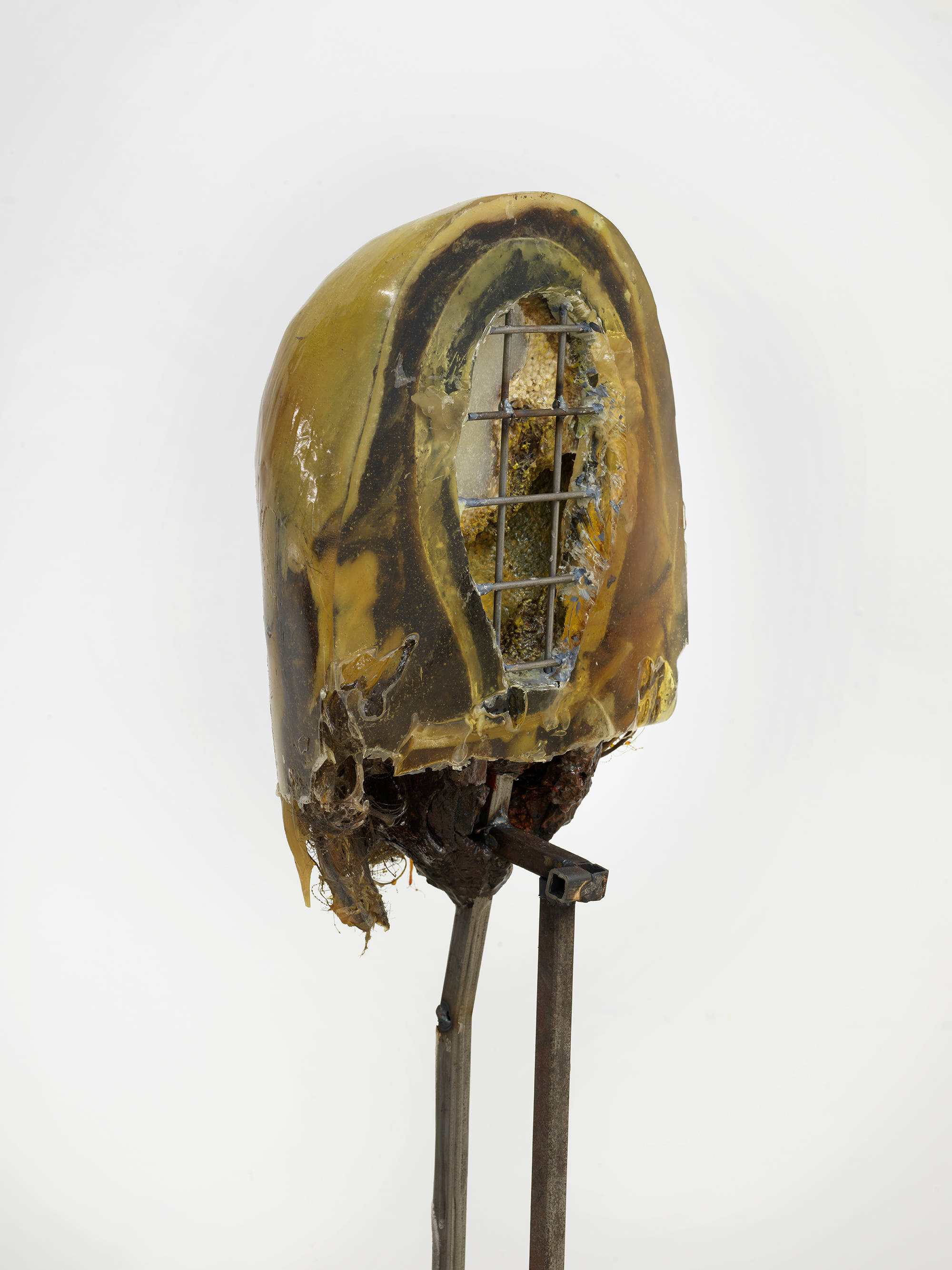 In a gallery space, a detail of an abstract sculpture resembling a human form with a steal base.