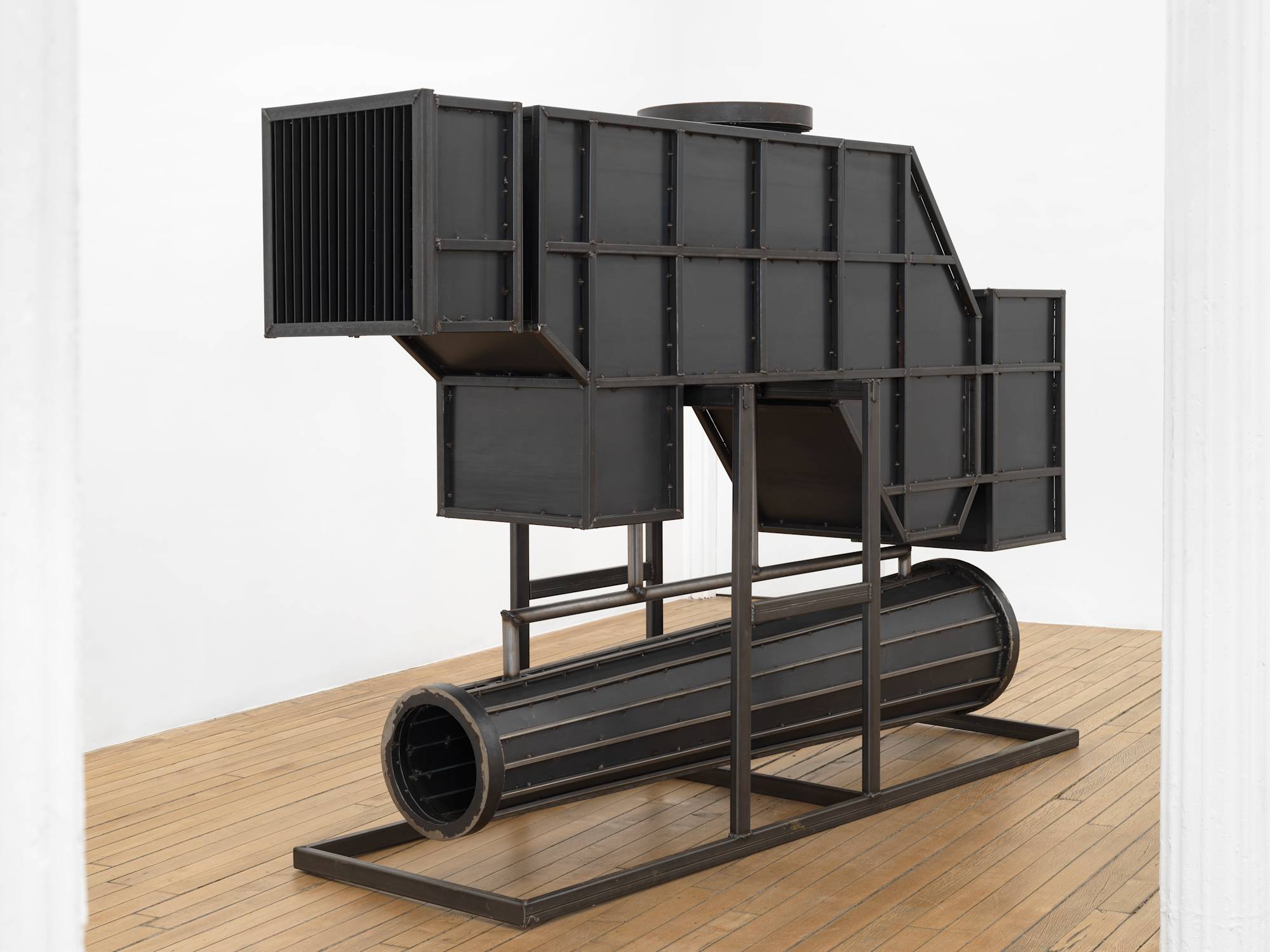 In a gallery space, a large steel sculpture resembling an abstract furnace.