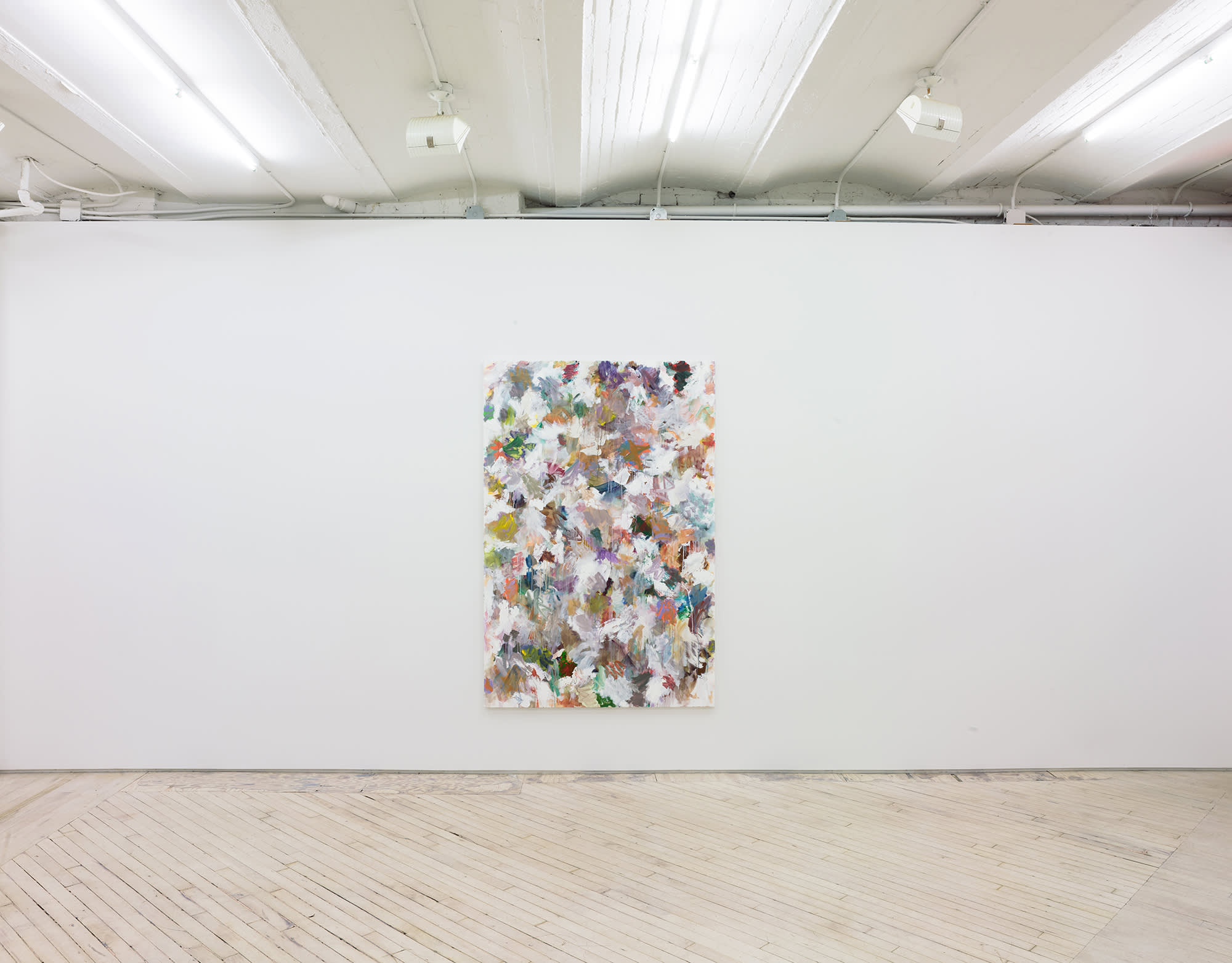 In a gallery space, a large abstract paintings is hung in the center of a large white wall. The painting contains numerous swatches of various colors painted on top of one another. The paint is thin and in some areas dripping.