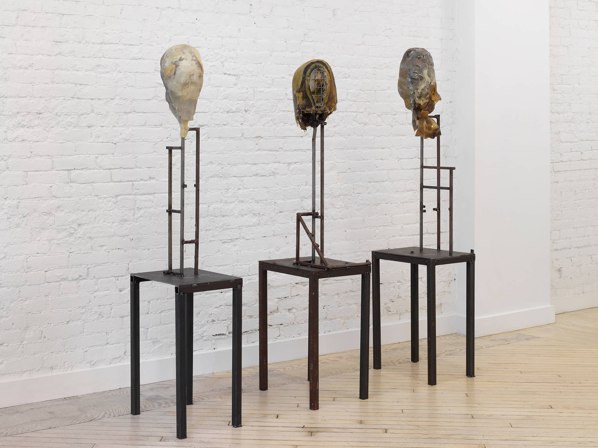 Three floor standing sculptures resembling mutilated human body parts on top of steel bases.