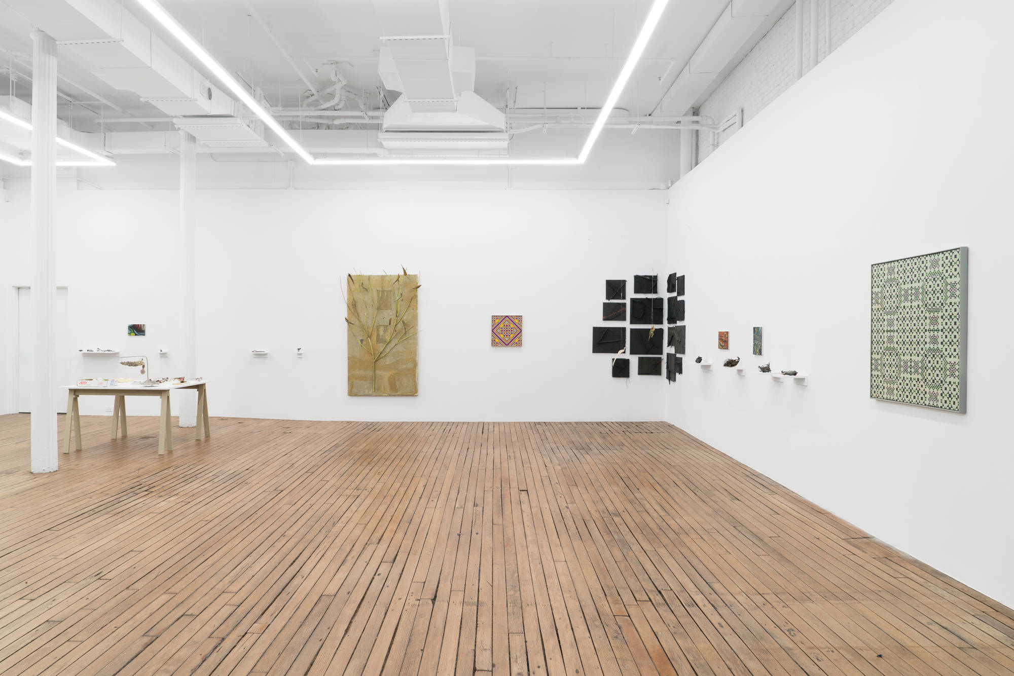 A mixture of abstract paintings and small sculptures hang on the walls of a brightly lit gallery with wood floors.