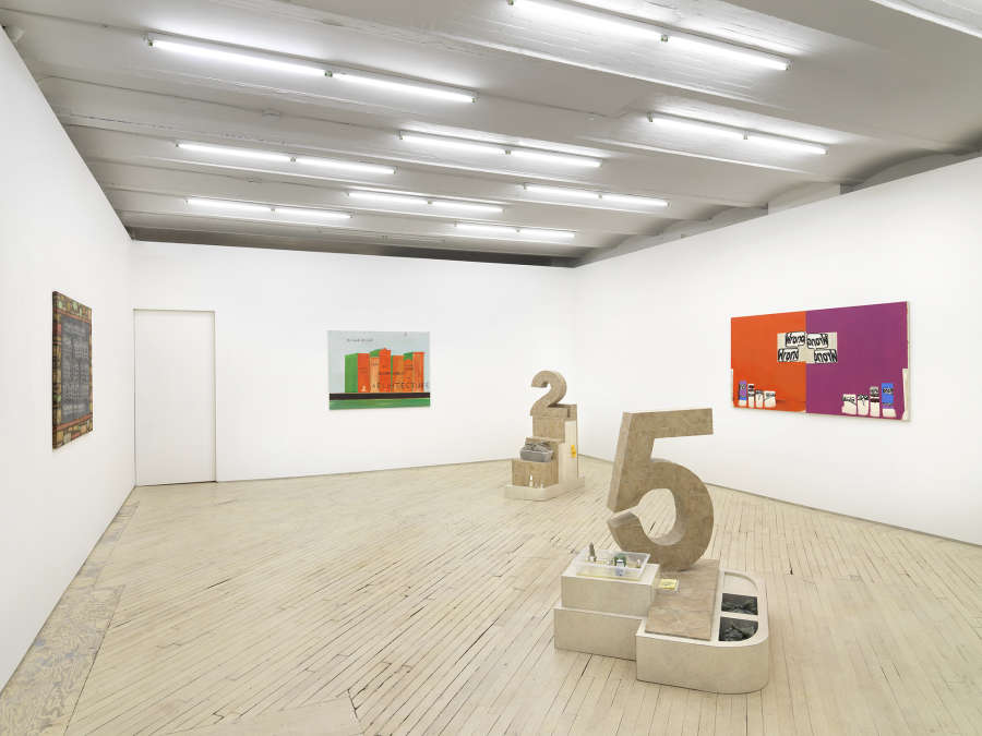 In a gallery space, three large paintings are hung on separate walls facing one another. The paintings are graphic and colorful. In the center of the room are two large numbers, "2" and "5", sculpted out of flooring tiles. The bases for the number sculptures contain numerous other small objects. 