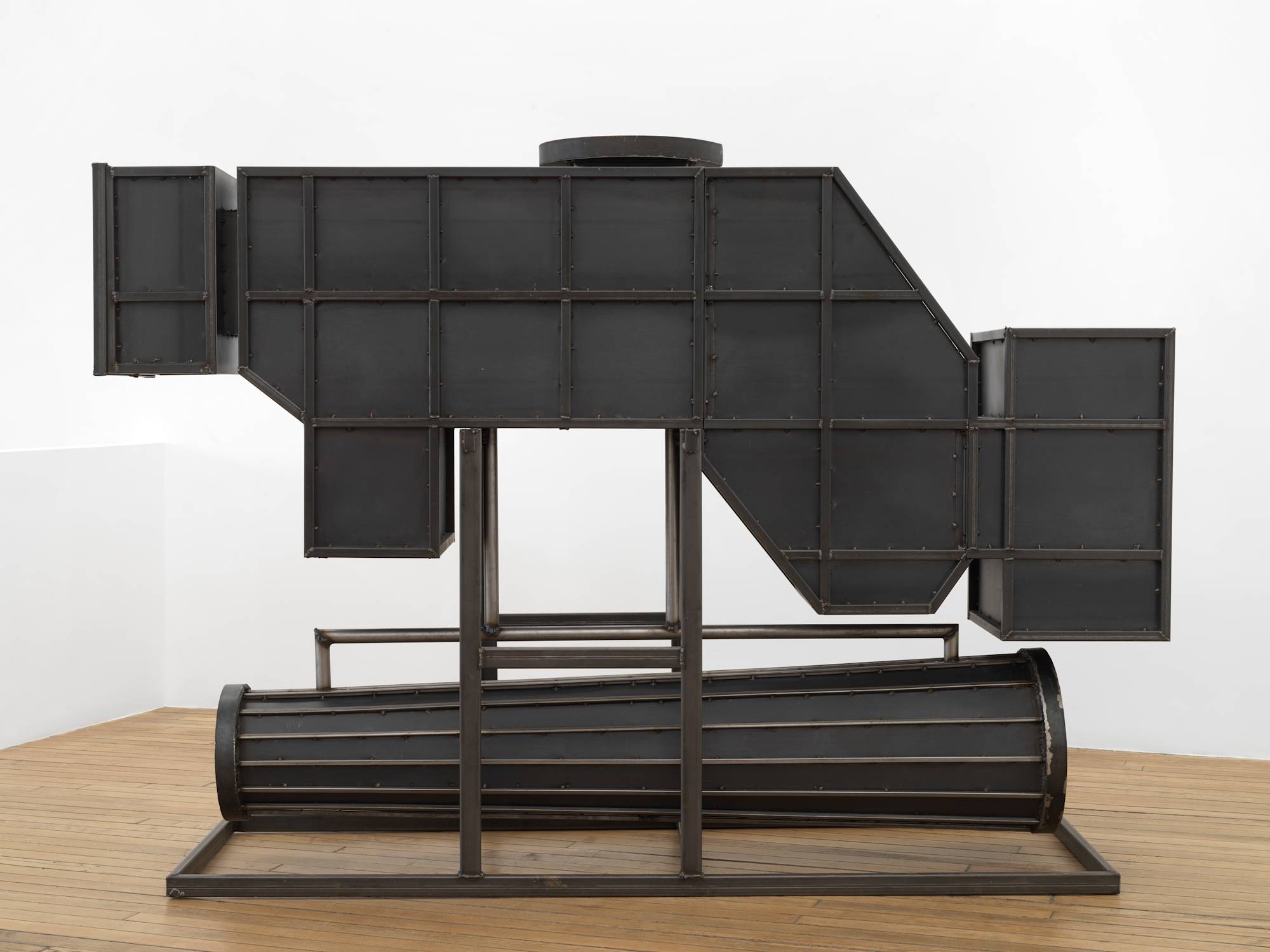 In a gallery space, a large steel sculpture resembling an abstract furnace.