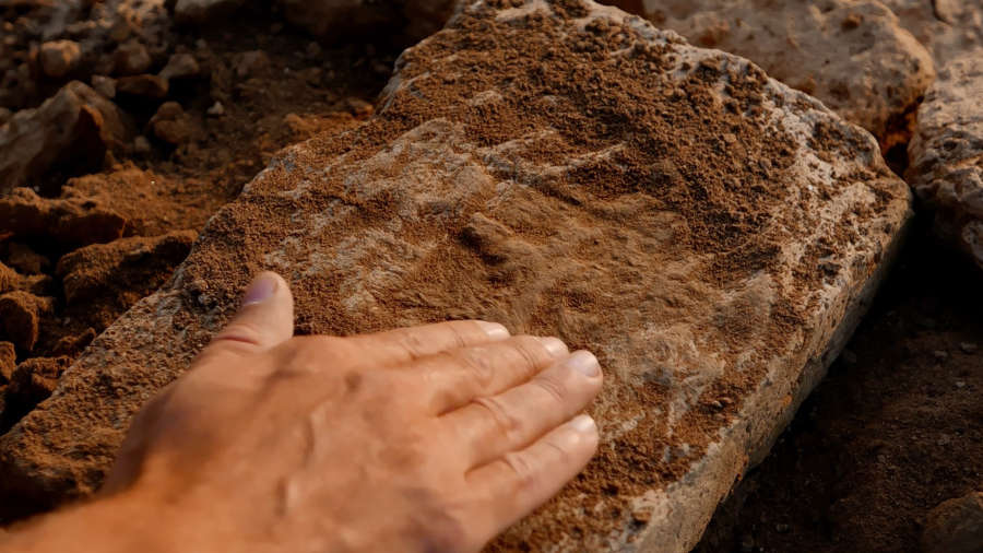 Still image from the animated film Thunderbird showing a live action image of a hand brushing dirt away from a buried artifact.