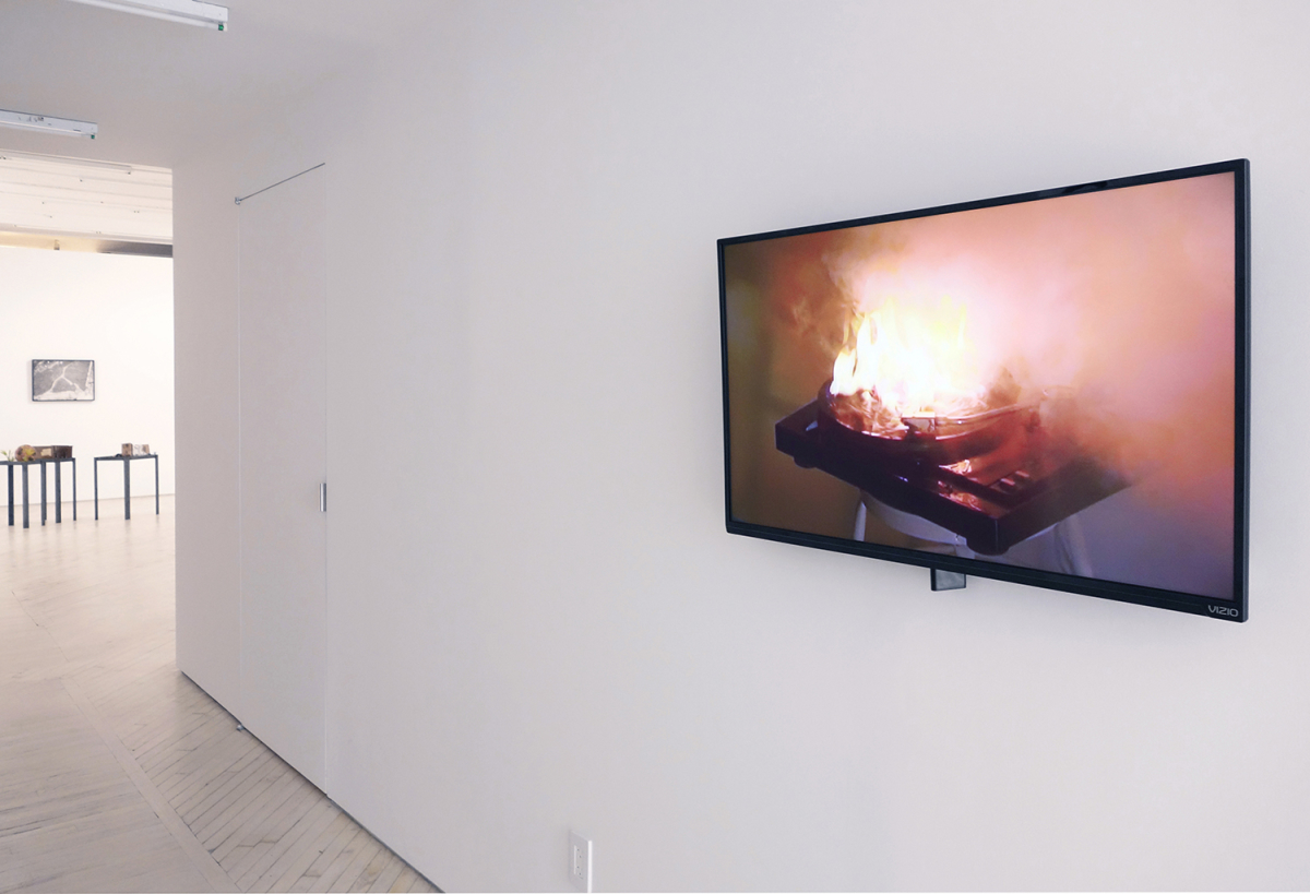 Installation view: Keren Cytter, Four Seasons, 2009, a video on a flat screen monitor on a white wall along a hallway leading into the gallery at the end with sculptures and wall works beyond.