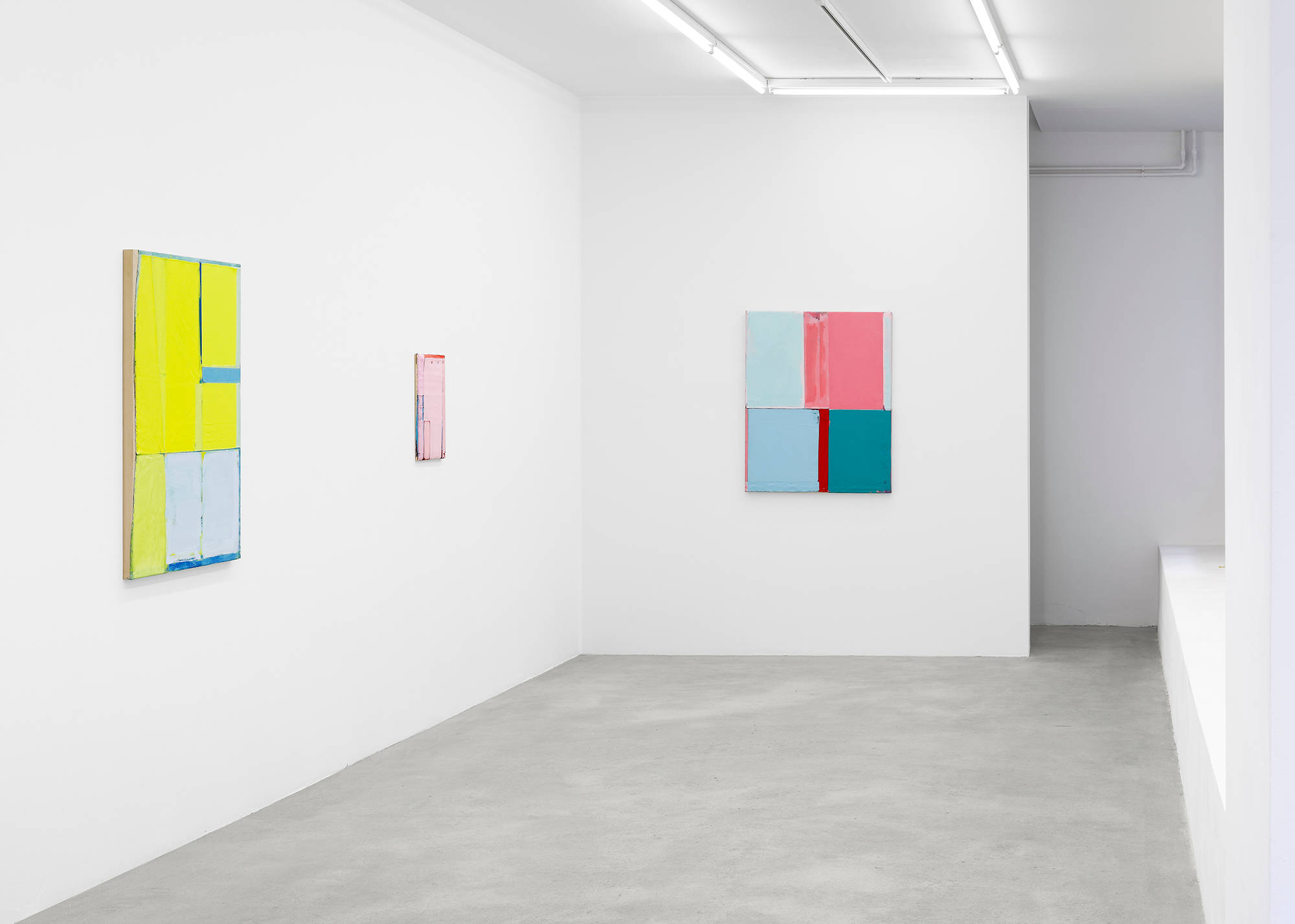 In a gallery space, three abstract paintings hung evenly spaced apart. The paintings are formally dominated by rectangular blocks of color. The paint to the left is a yellowish-green. The smaller painting in the middle is primarily pink. The painting on the right is a hue of pink, green, and blue. The paint is very thick and the canvases are rough.