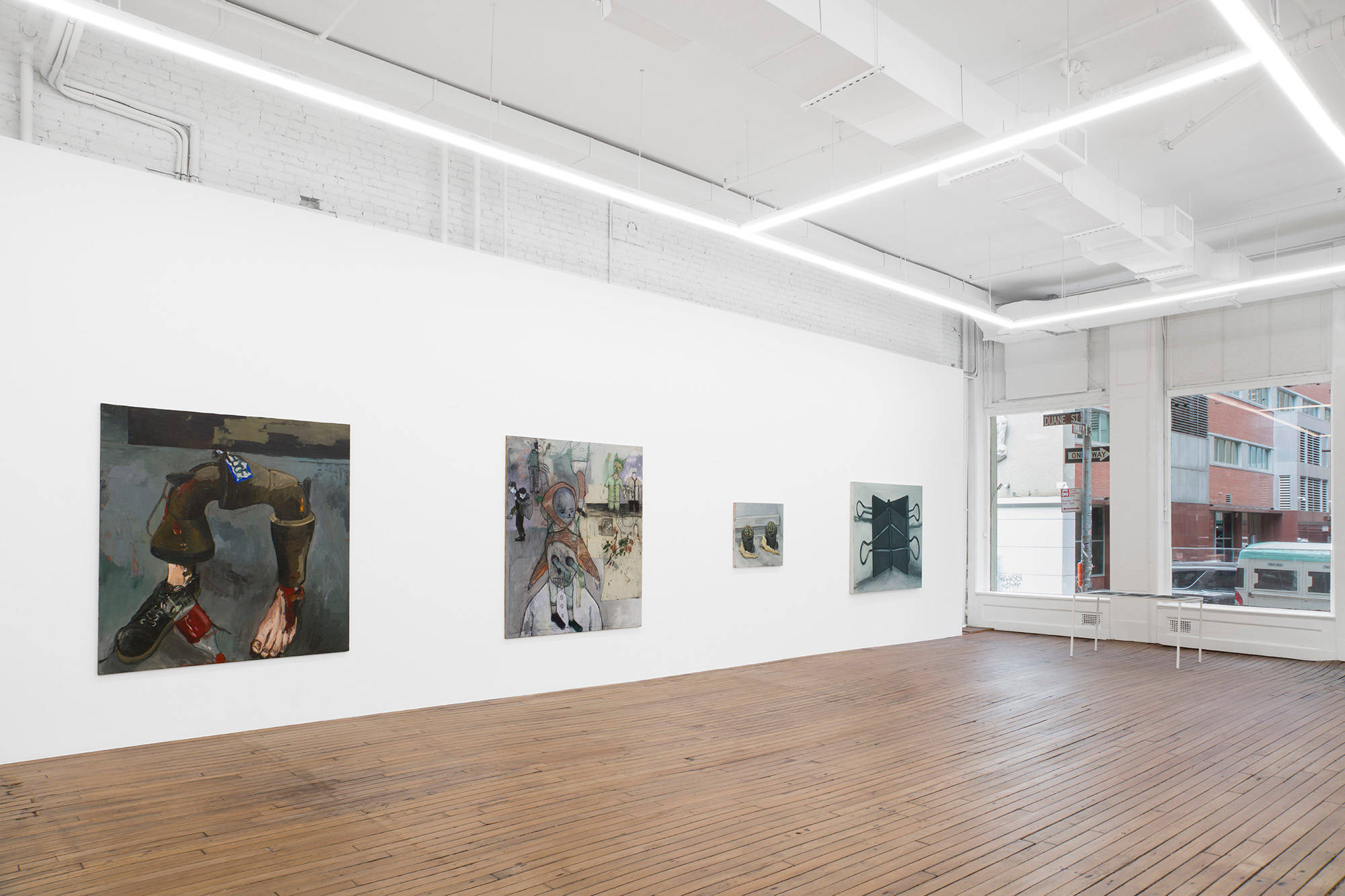 Four paintings including disembodied feet, cacti, and binder clips hang on the West wall of the gallery and a table with six drawings sits against the windowed North wall. The drawings are not visible due to their angle to the camera.