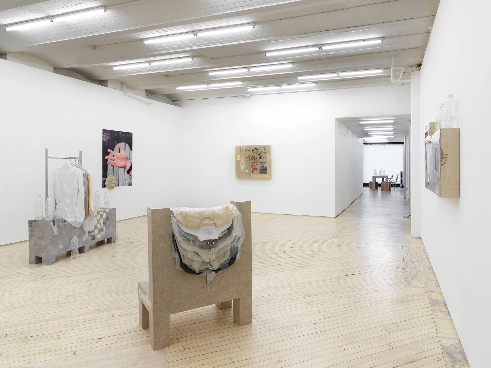 Gallery view with multiple sculptures on view, as well as 2D works hanging on the wall. A hallway is on the right, leading down to the front of the gallery where another sculpture is visible.