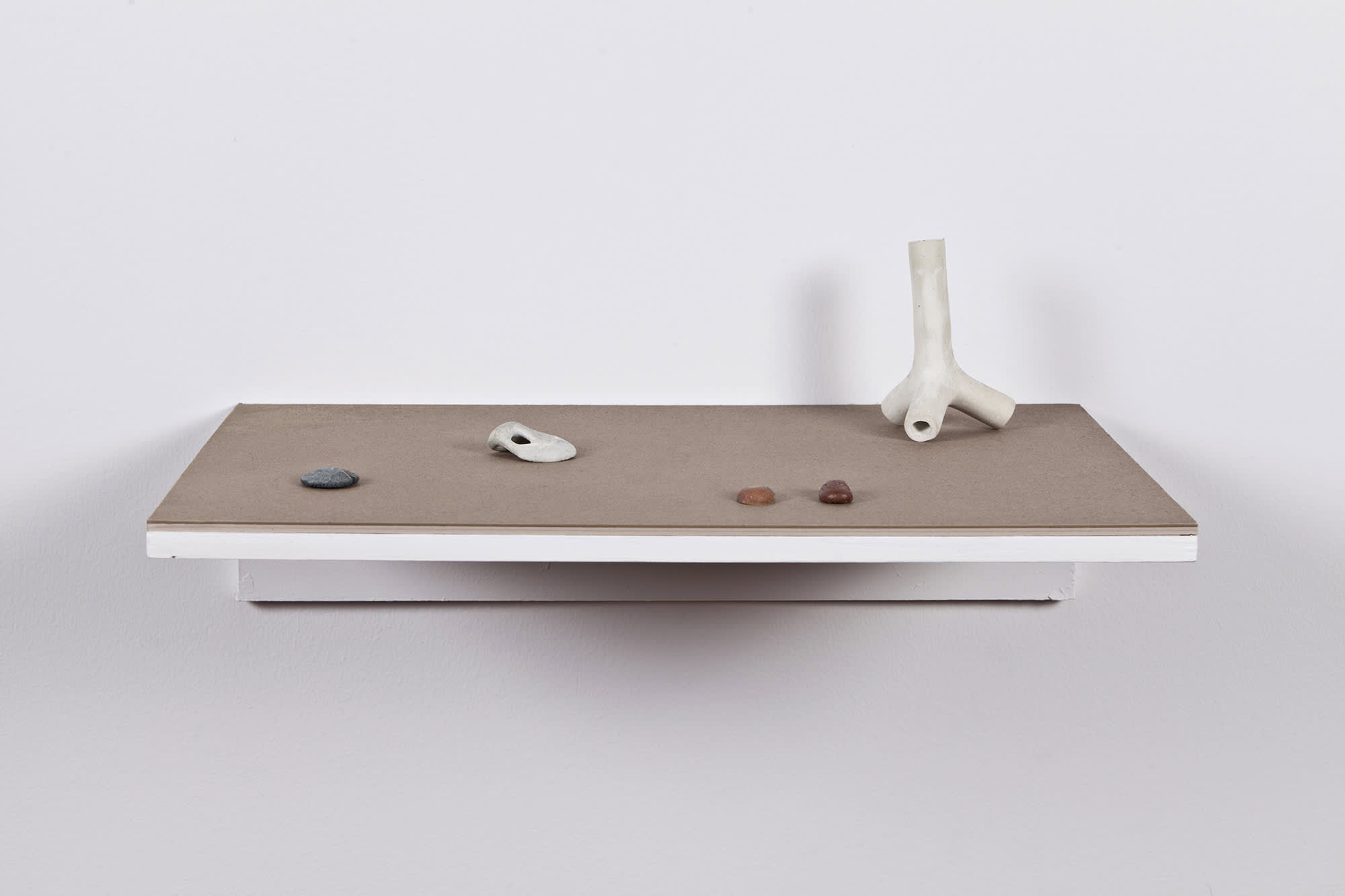 On brown wall-mounted shelf, several miniature abstract sculptures resembling bones or rocks.