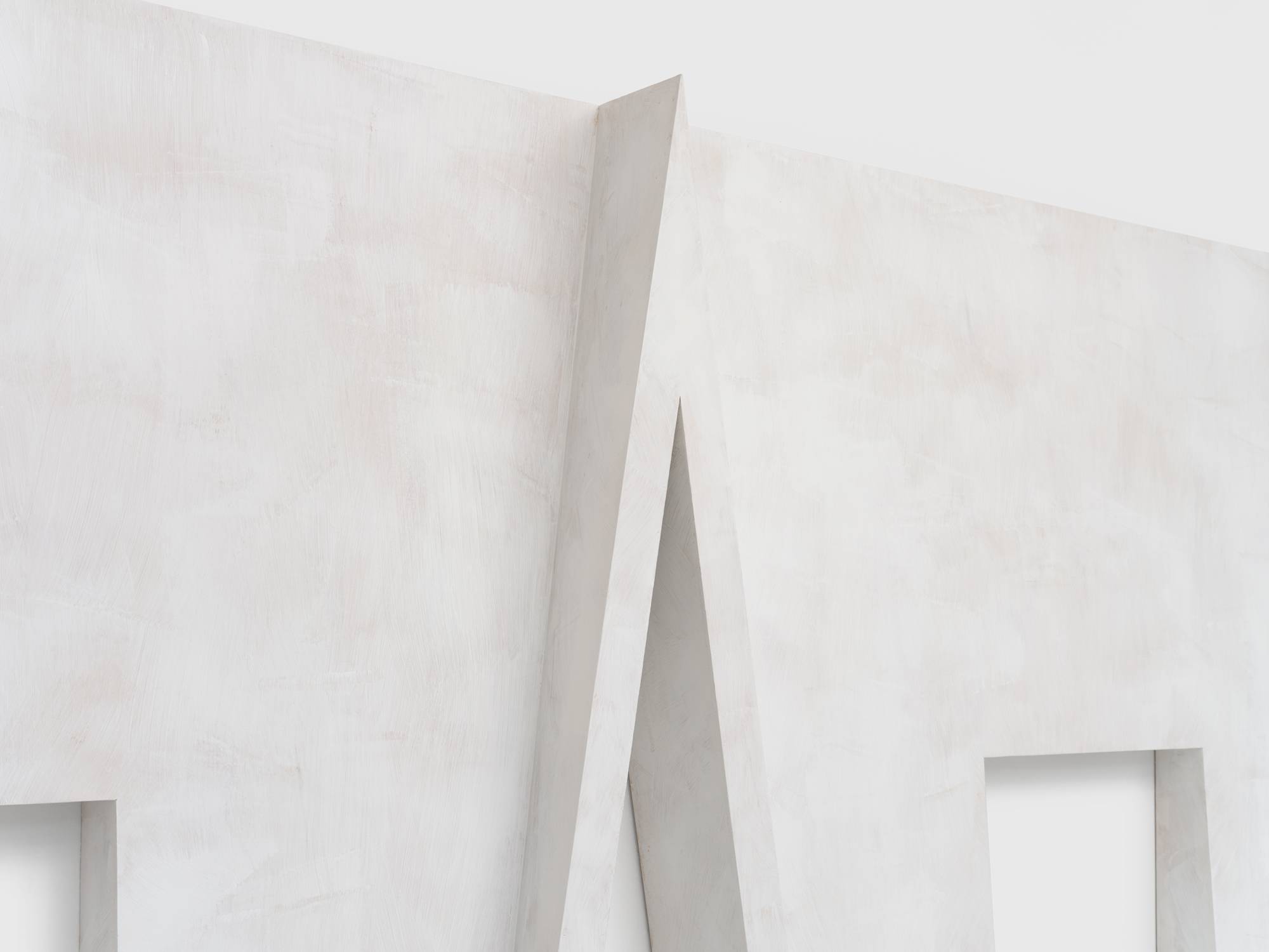 Detail of a large wall sculpture designed with a gently receding slope from bottom to top with two rectangular window cutouts on either side. The center features a cutout resembling a cross gable roof.
