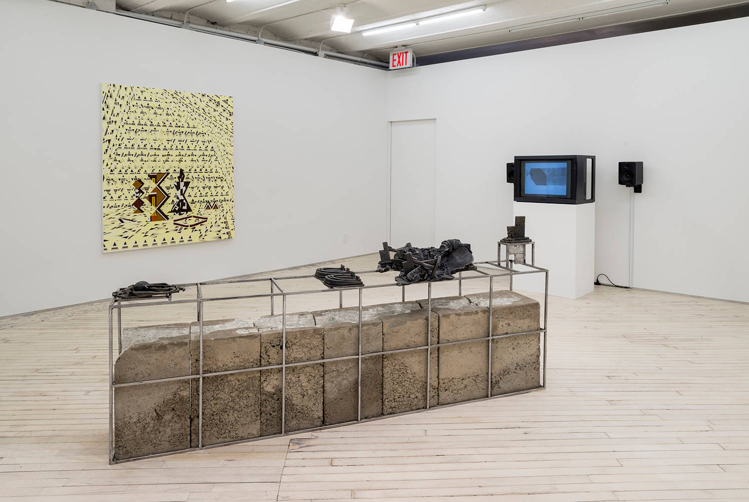 Installation view of the exhibition in the main space. At left, a yellow and brown painting by Farah Atassi, in the foreground a low concrete and metal sculpture by Lionel Maunz, and in the back right, a monitor on a plinth plays a video by Wojciech Bakowski.