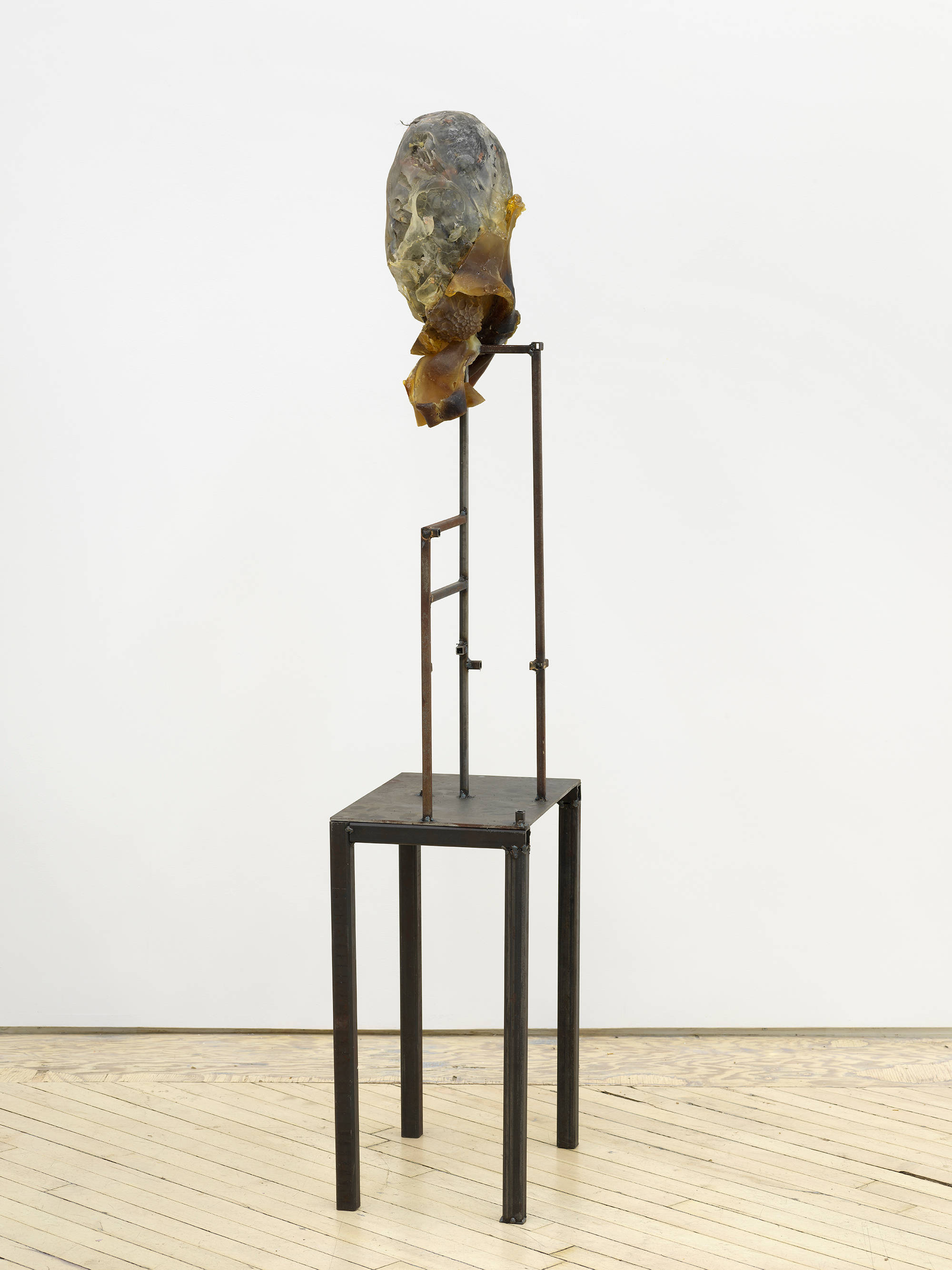 In a gallery space, an abstract sculpture resembling a human form with a steal base.