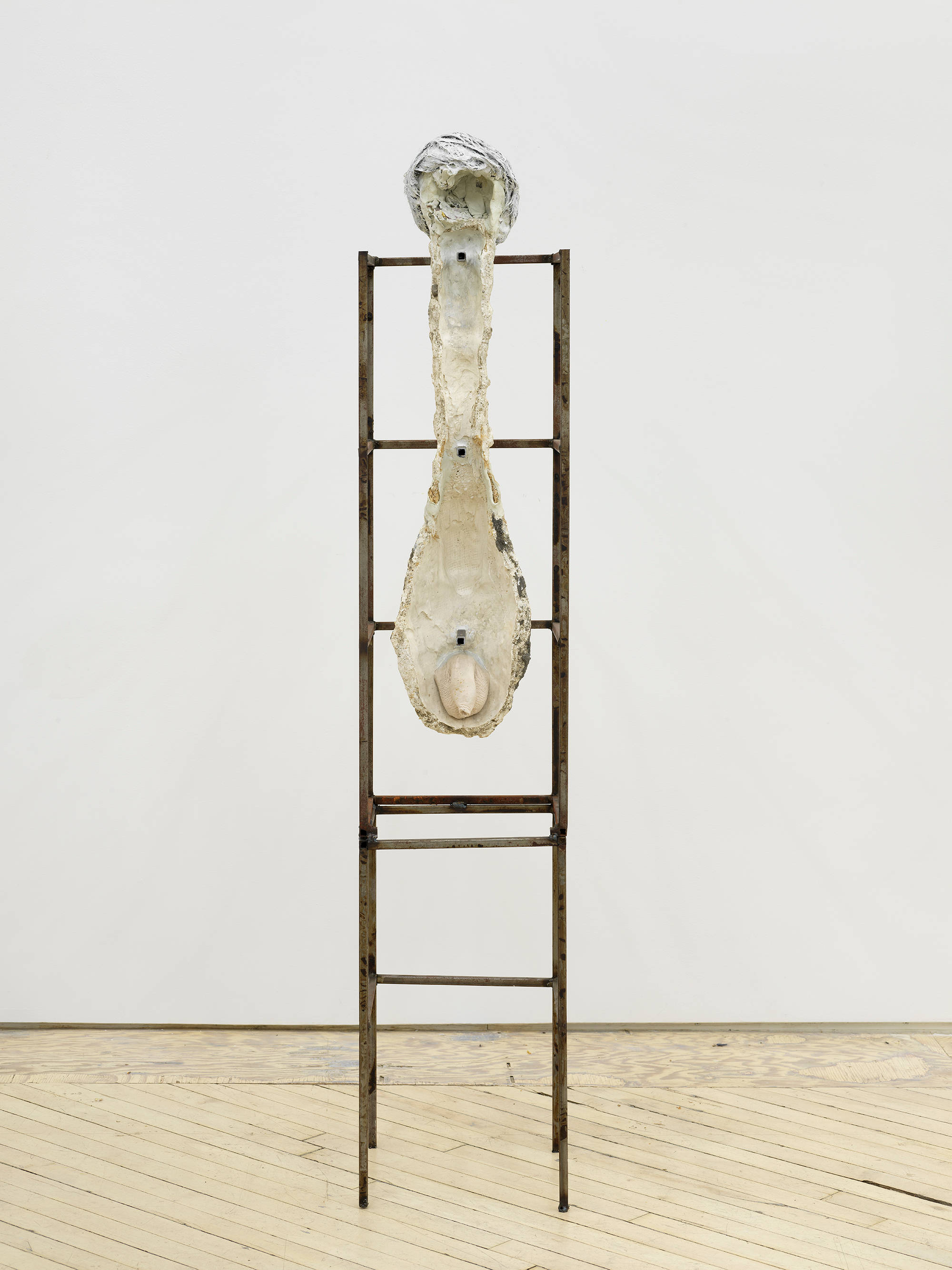 In a gallery space, an abstract sculpture resembling a human form with a steal base.