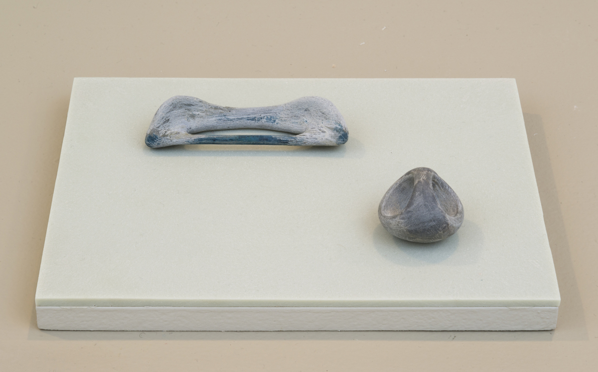 Two small sculptures resembling bones or other organic matter on top of an green-tinted plinth.
