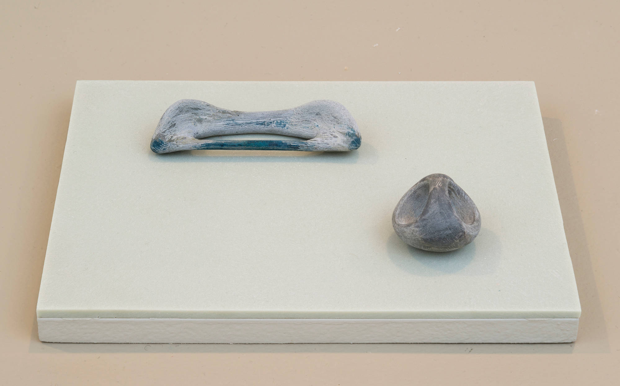 Two small sculptures resembling bones or other organic matter on top of an green-tinted plinth.