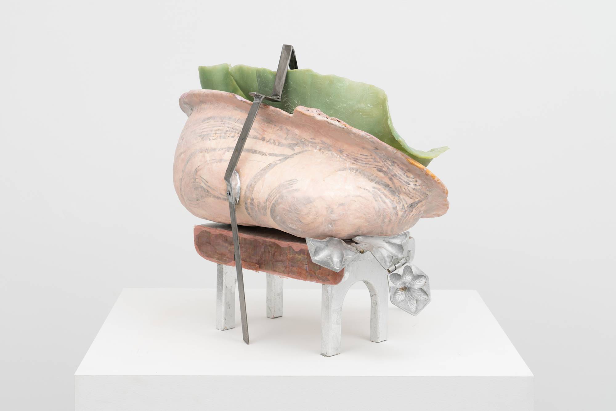 Rear view of an Em Rooney sculpture featuring a stool wrapped in foil and mother of pearl, supporting a hinged steel mold of a flower, a pink fiberglass mold of an arm and a thin green silicone cast. A thin strip of bent steel is draped over the sculpture.