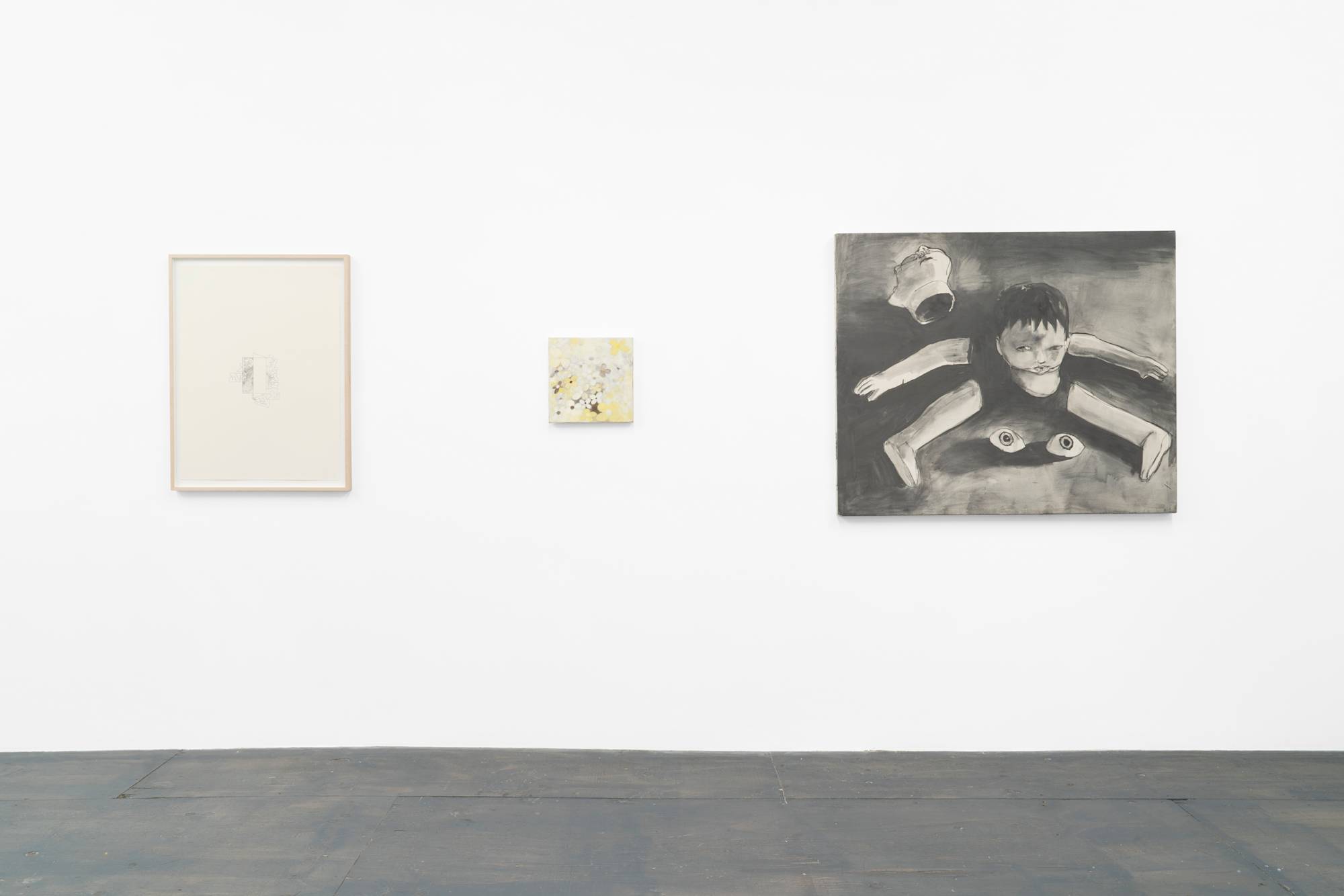 Three artworks hang in a row above a grey wood floor. One graphite drawing in wood frame, one small, abstract, yellow flower painting, and one liquid graphite painting depicted a dismembered boy.