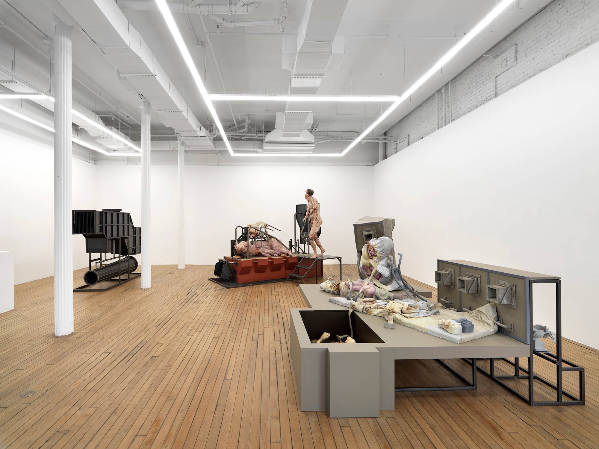 A large gallery space filled with three monumental sculptures. A figure and giant pig rest on top of a platform in the back, a large steel structure on the left.