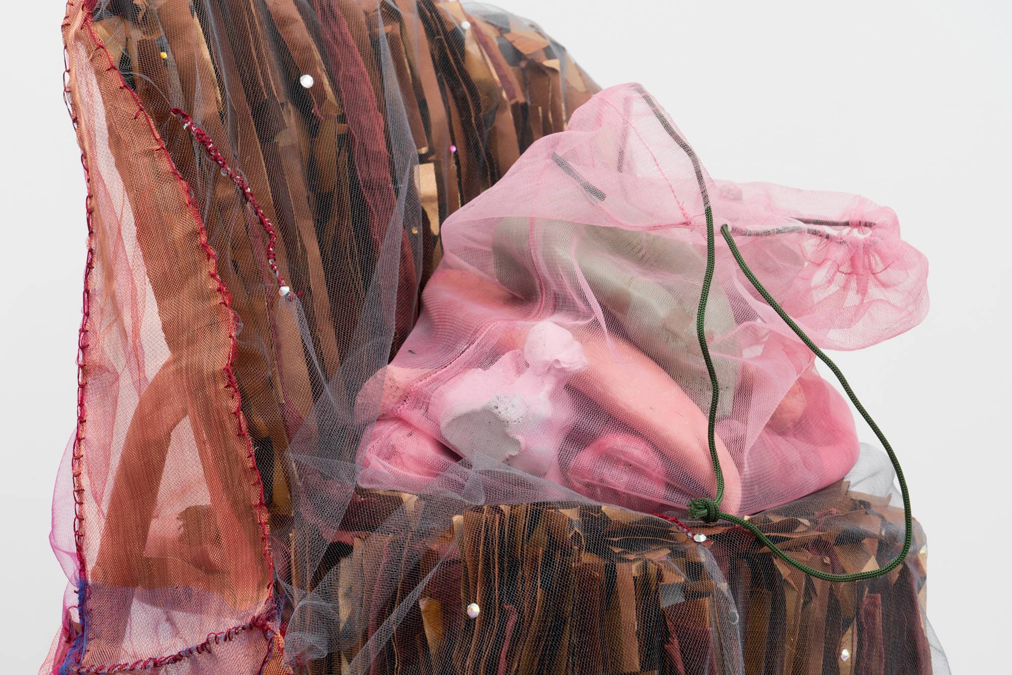 Detail of Em Rooney sculpture of a red children's folding chair adorned with mesh, folded paper, and resin-cast fruit.