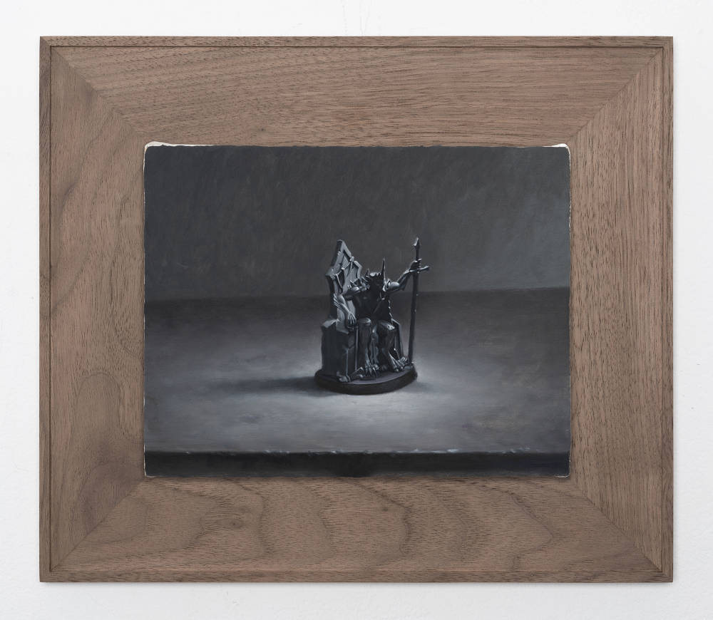 A small still life painting of a medieval figurine painted in a range of grays in a wooden frame. 