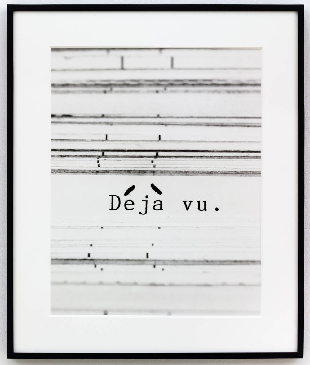 A black and white framed vertical photograph with a white background and horizontal black lines and at center, the type written phrase, 'Déjà vu.' The accent marks are hand written.