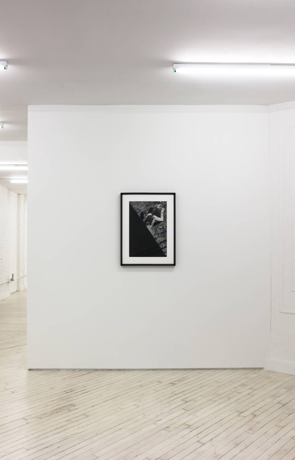 Image of the front gallery, a black and white framed photo hangs center on the wall. The photo has the bottom left triangular totally black and coming out from under that is a soiled body face down in the mud.