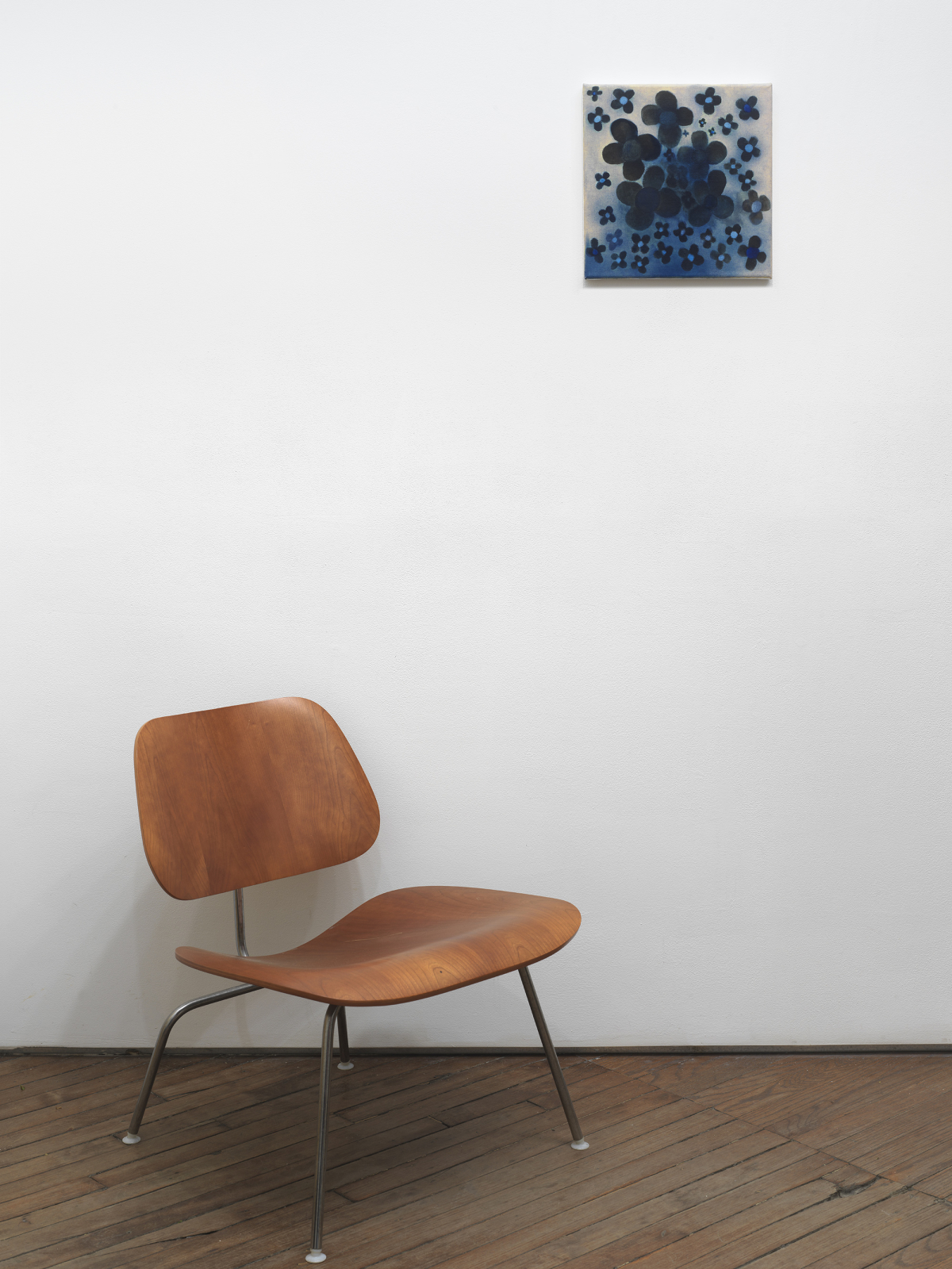 A small square abstract painting depicting graphic flowers in black and blue. Below is a chair. 