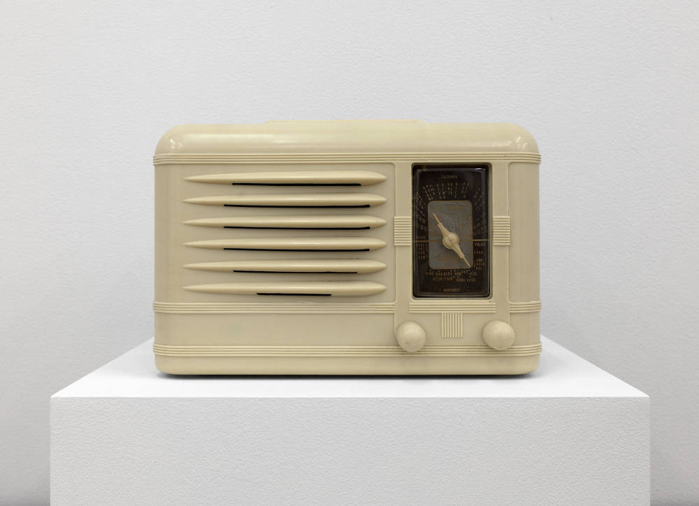 A cream-colored vintage radio placed on top of a white pedestal. 