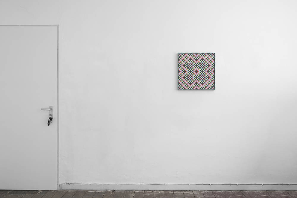 Image of a colorful grid painting installed on a wall. The the left is a door that has a key left in the lock. 