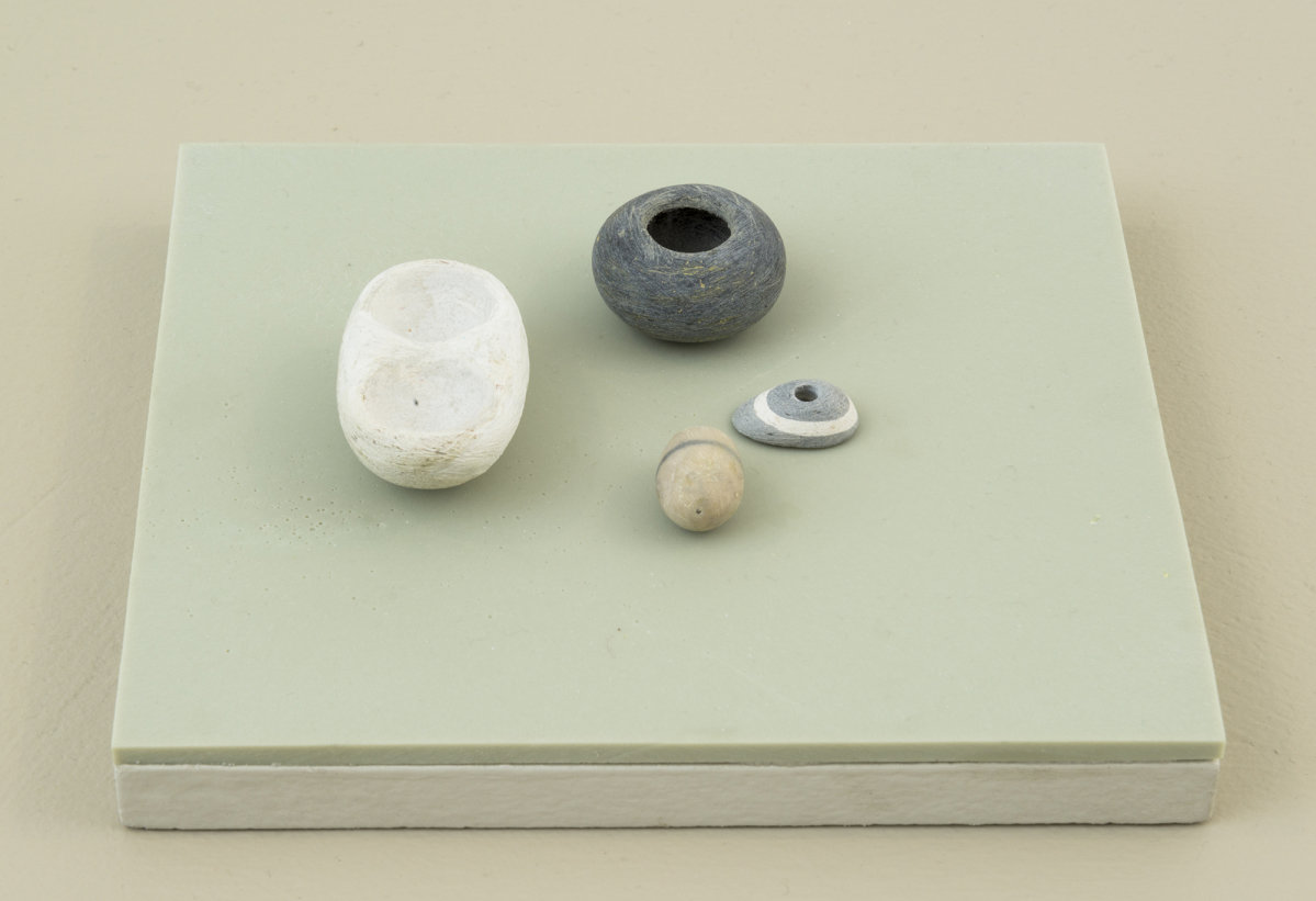 Four miniature sculptures resembling organic forms resting on top of a green-tinted plinth.