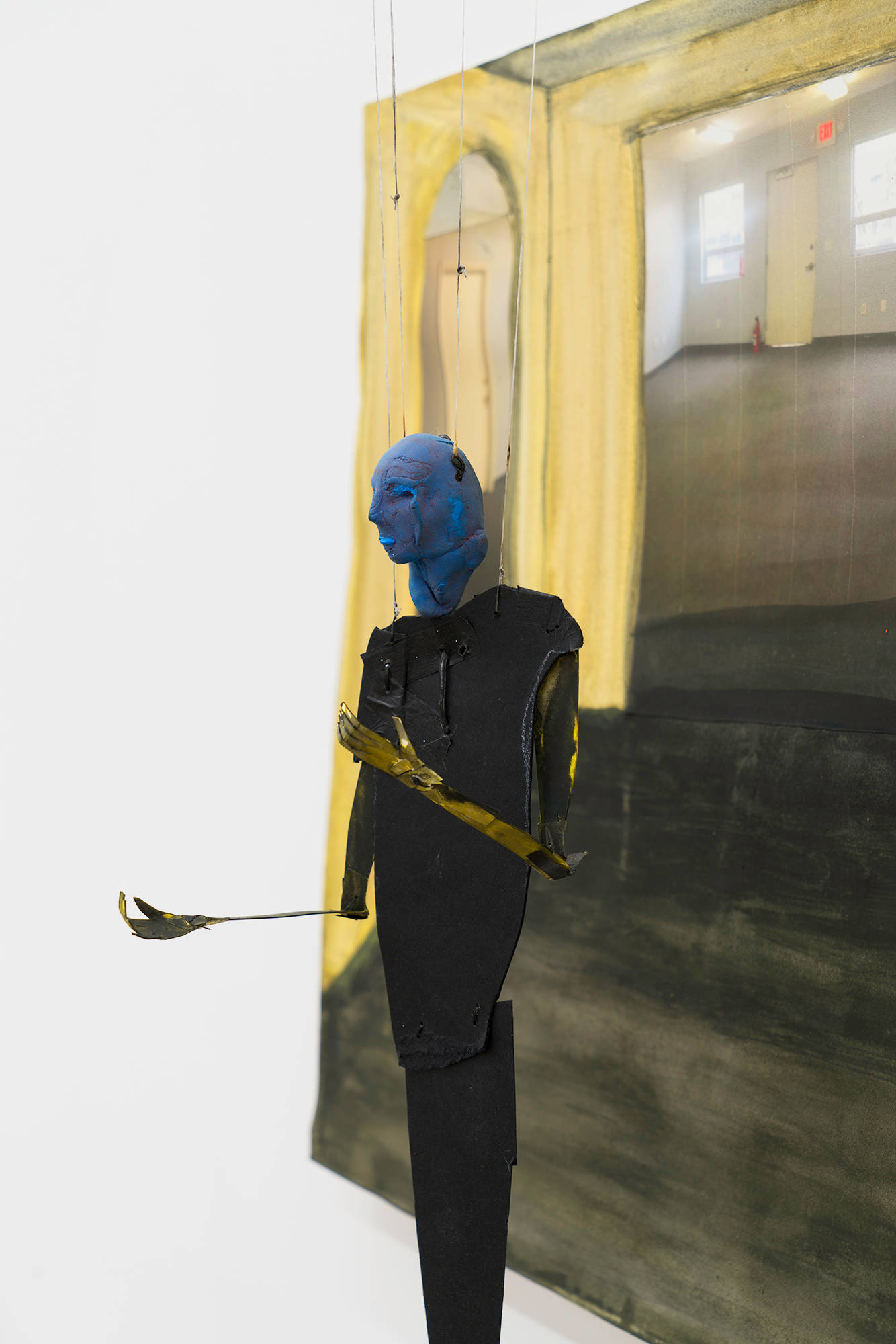 A detail shot of blue puppet in front of collaged room.