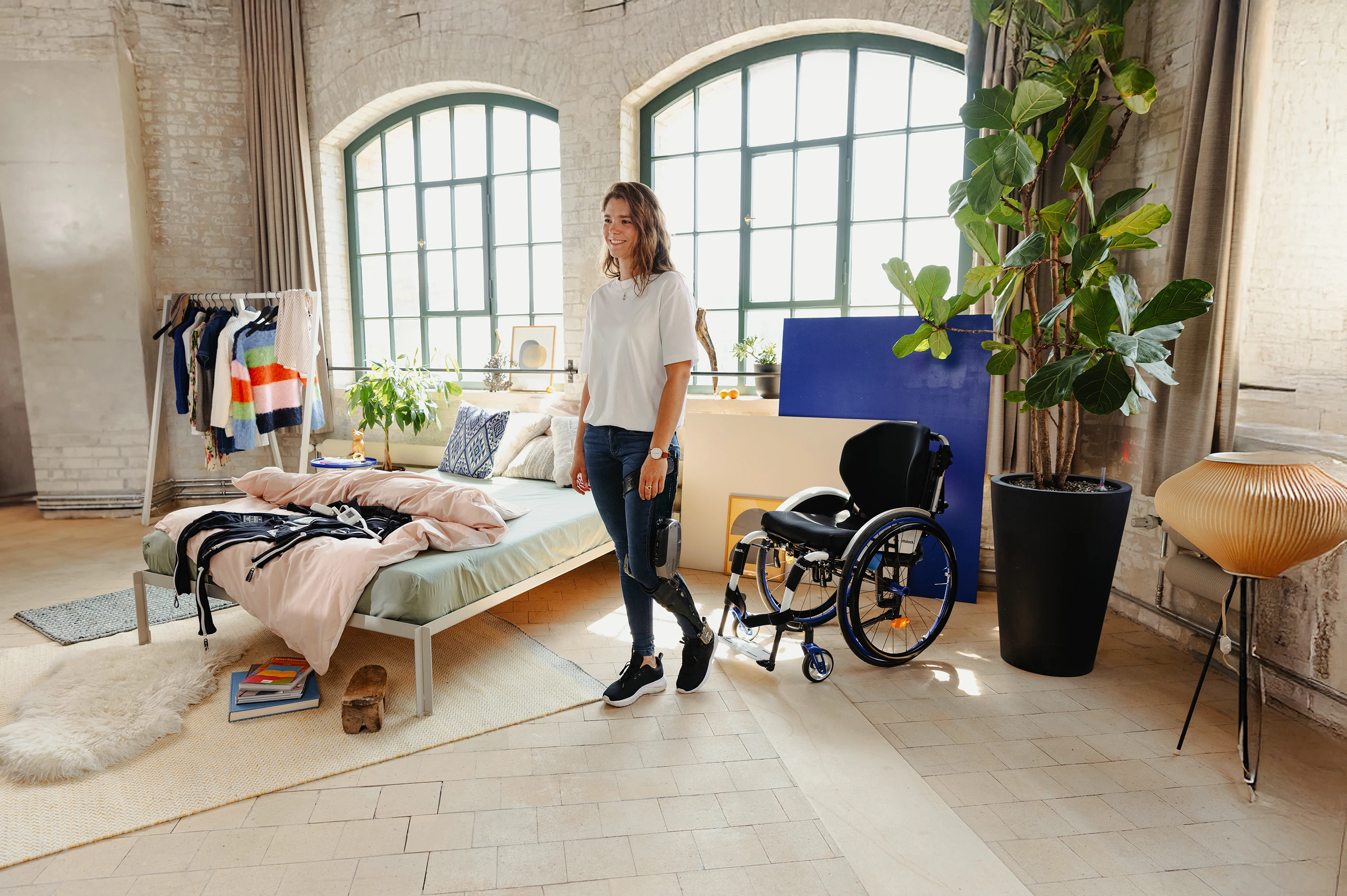 Person standing next to a wheelchair in a room with large windows, plants, and clothing racks.